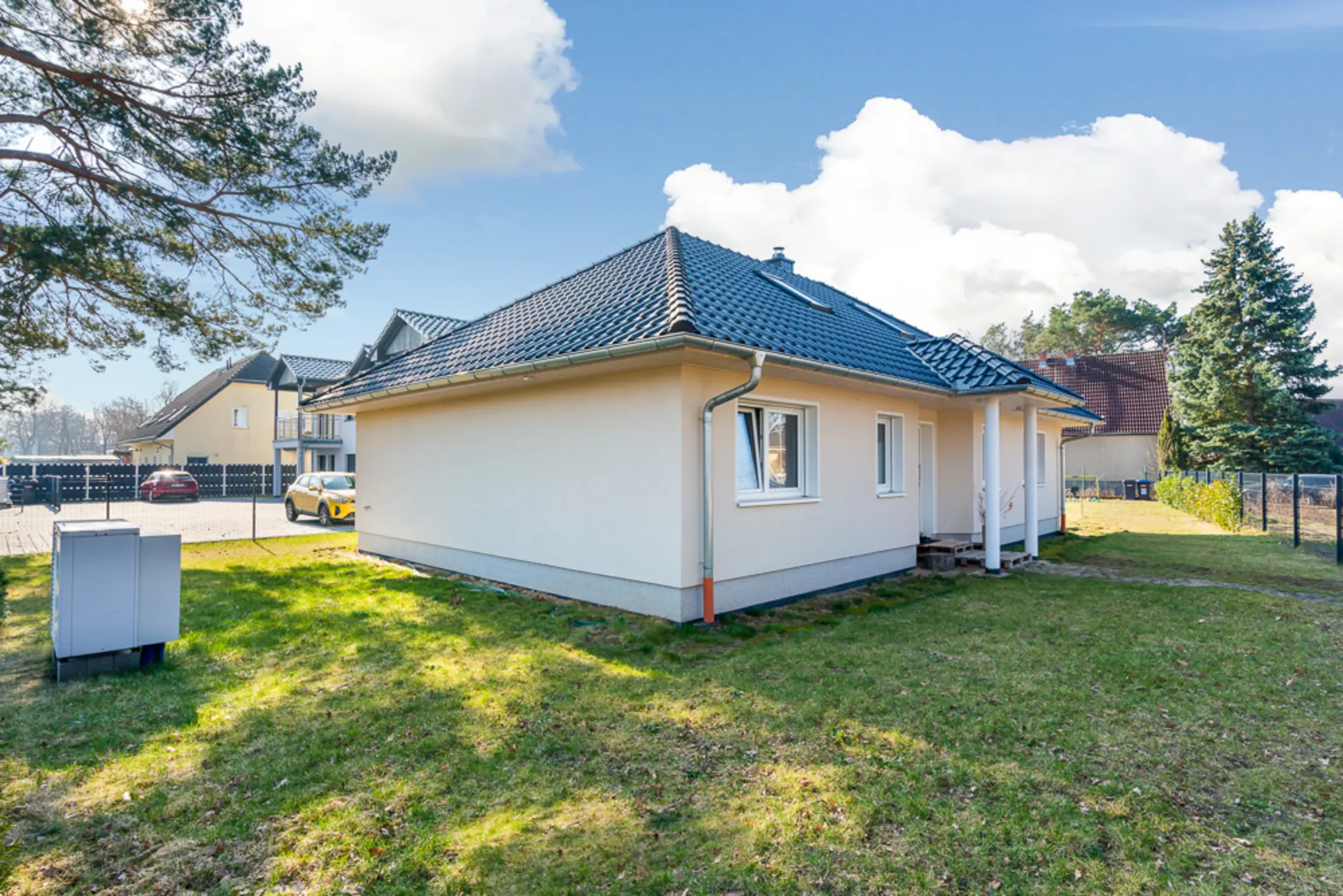 Einfamilienhaus mit hellem Putz, dunklem Dach und kleinem Garten bei sonnigem Wetter.