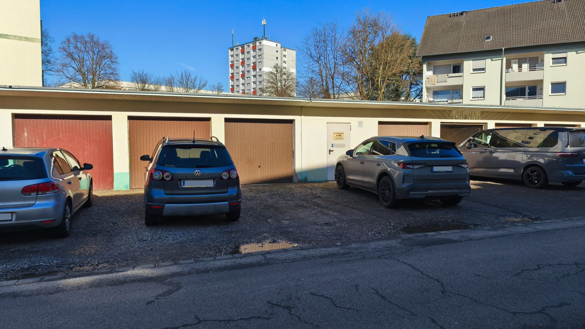 Vier Autos parken vor einer Reihe von Garagen neben einem Wohngebäude.