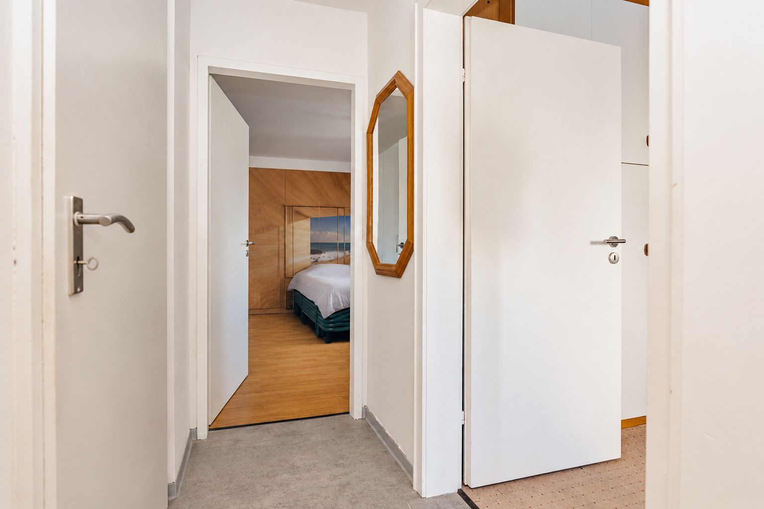 Flur mit geöffneten Türen, Spiegel an der Wand und Blick in ein Schlafzimmer.