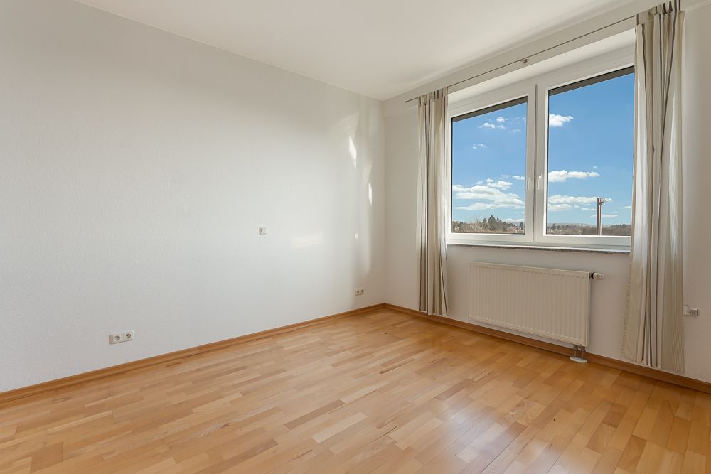 Leerer Raum mit hellem Holzboden, großem Fenster, weißen Wänden und Heizkörper unter dem Fenster.