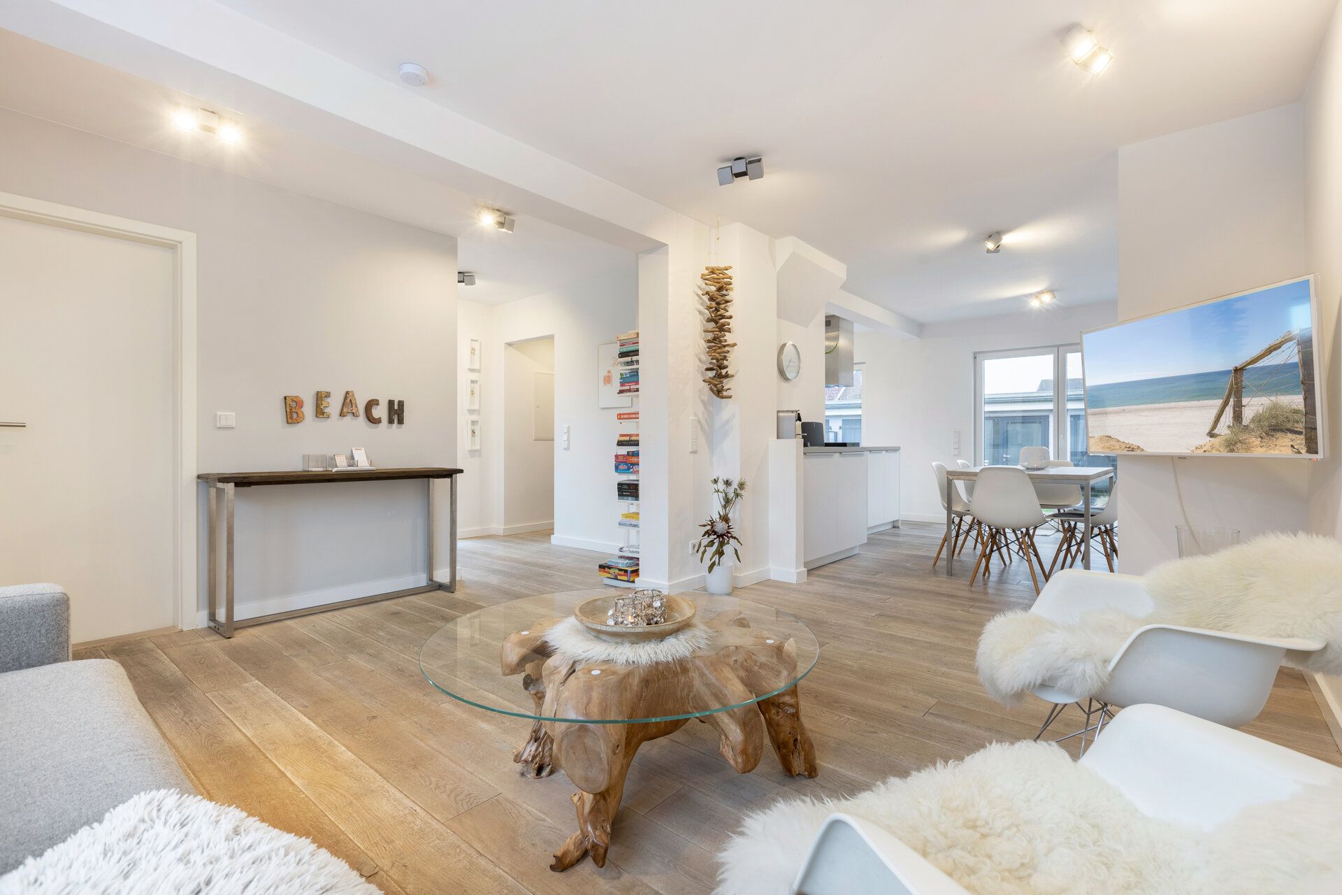 Helles Wohnzimmer mit Holzboden, Glas-Couchtisch und Blick auf Essbereich und Küche.