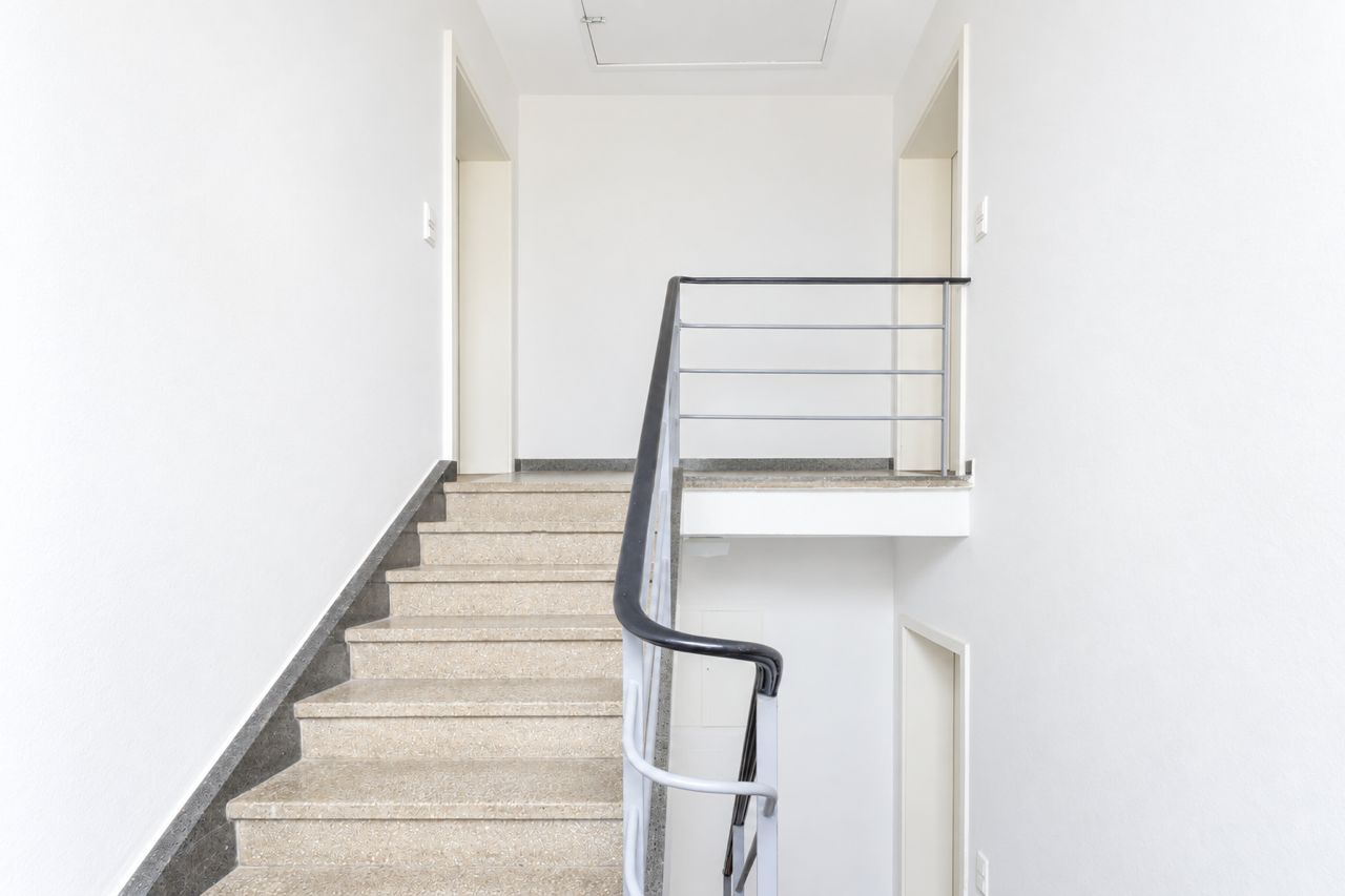 Helle Treppe mit Metallgeländer und weißen Wänden in einem Wohnhaus.
