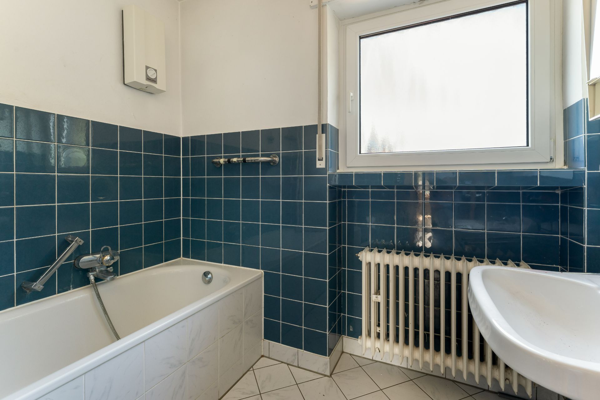 Badezimmer mit Badewanne, Waschbecken, blau gefliesten Wänden und Fenster.