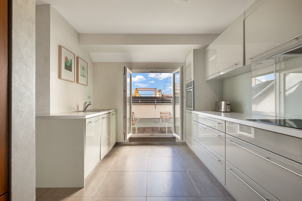 Moderne Küche mit weißen Schränken, zwei Bildern an der Wand und Zugang zu einem Balkon mit zwei Stühlen.