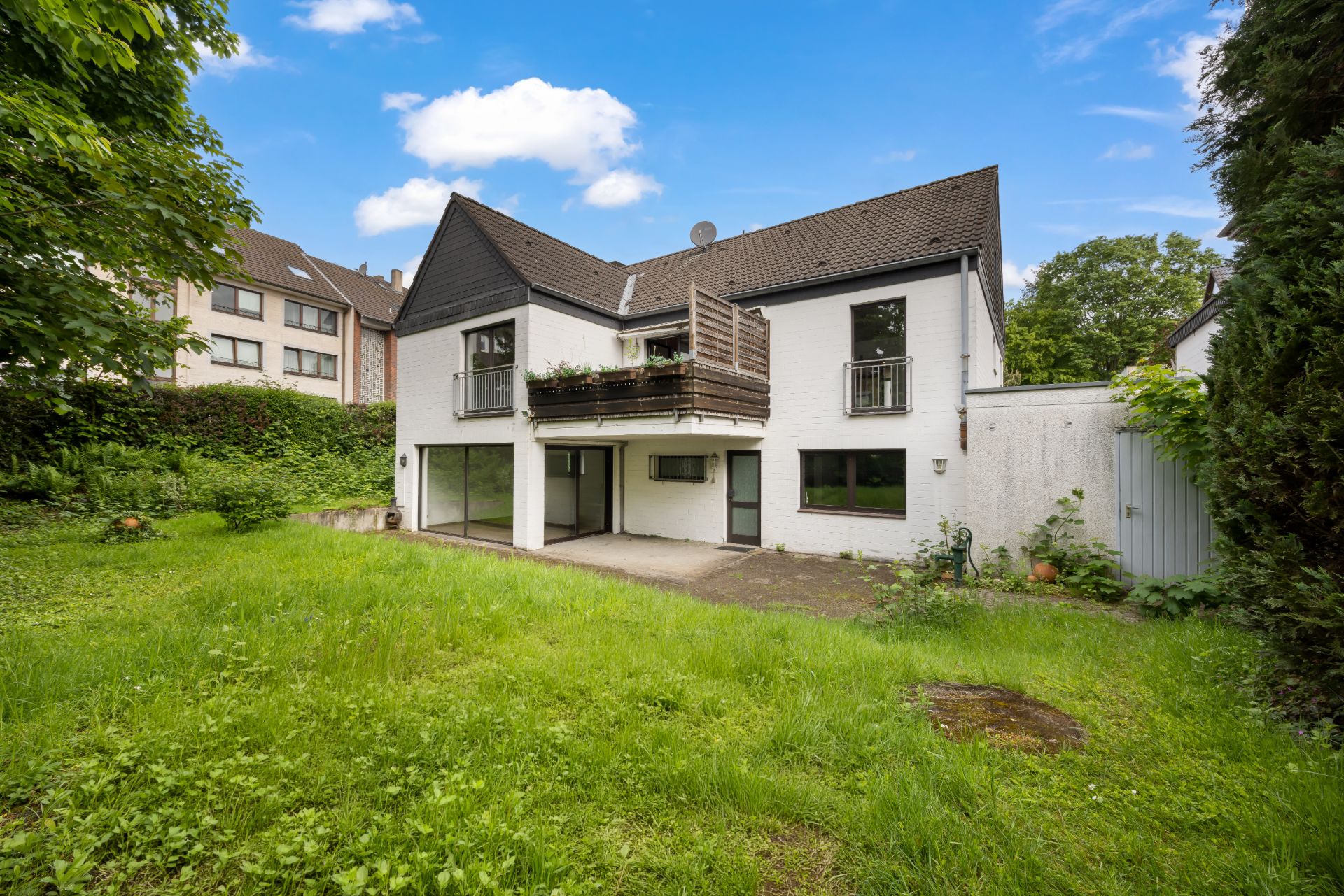 Weiße zweistöckige Wohnhaus mit Balkon und großem Garten bei sonnigem Wetter.