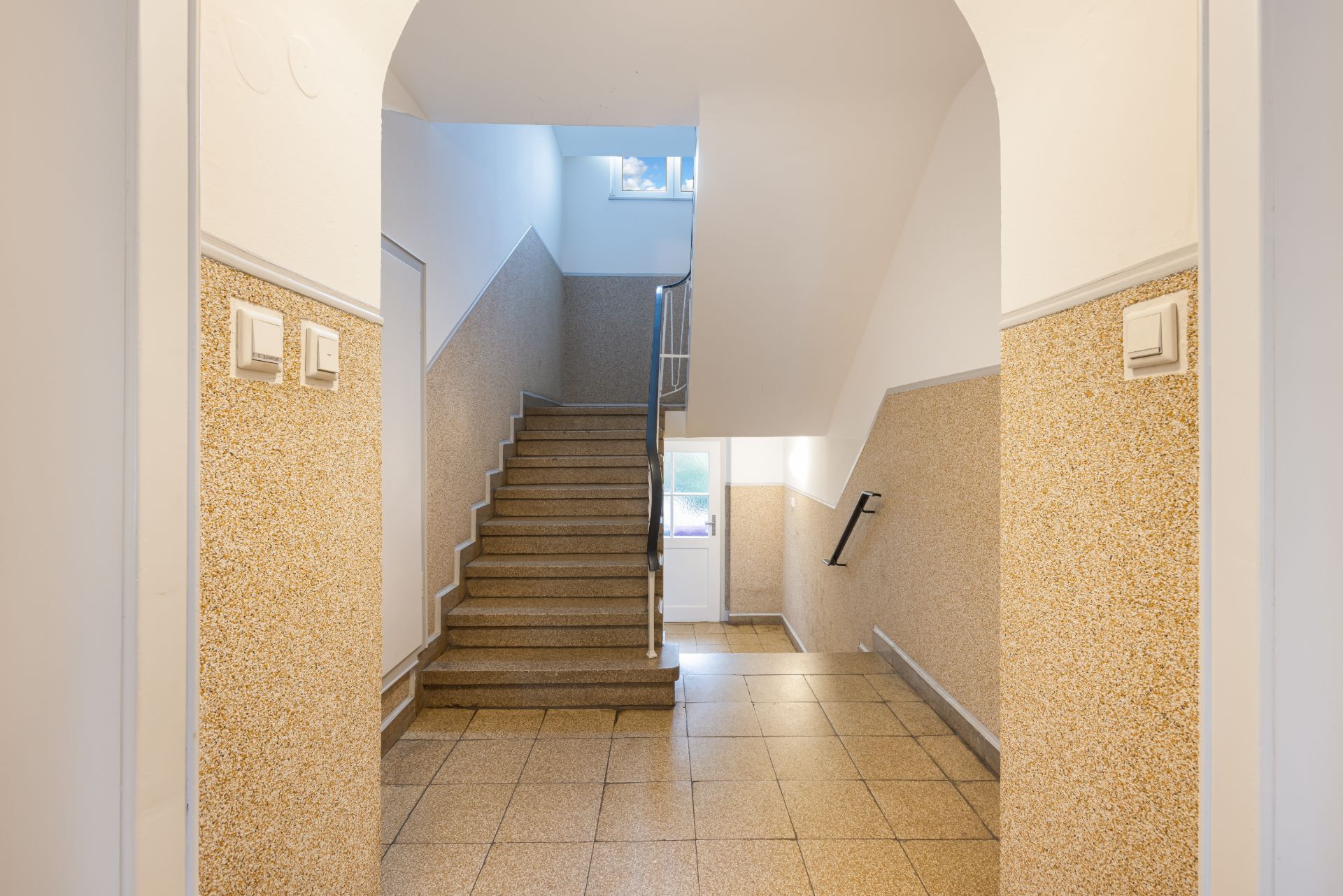 Helles Treppenhaus mit Fliesenboden und Geländer in einem Wohngebäude.