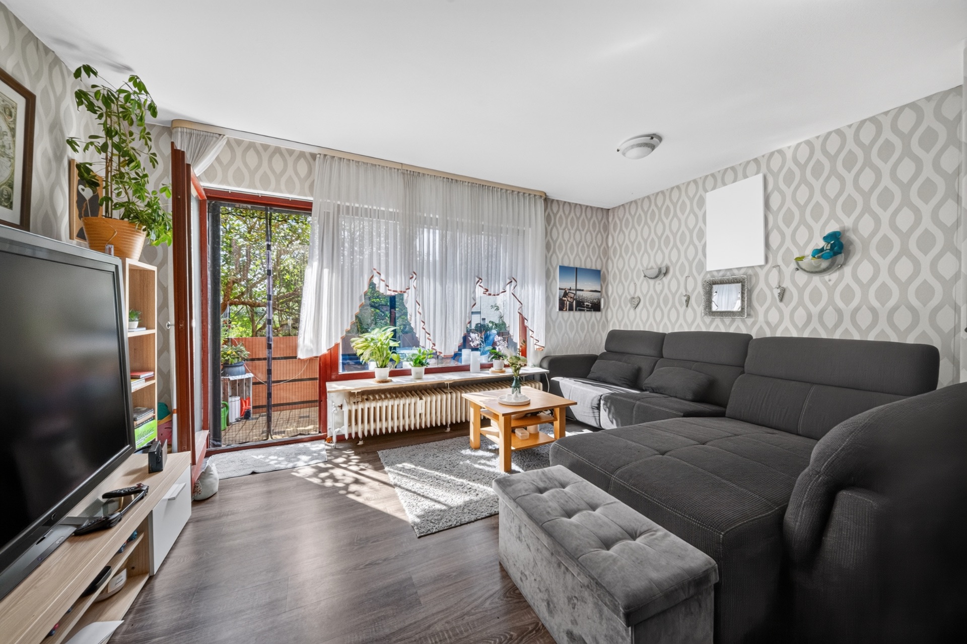 Wohnzimmer mit großer Eckcouch, Fernseher, Couchtisch und Zugang zu einem Balkon.