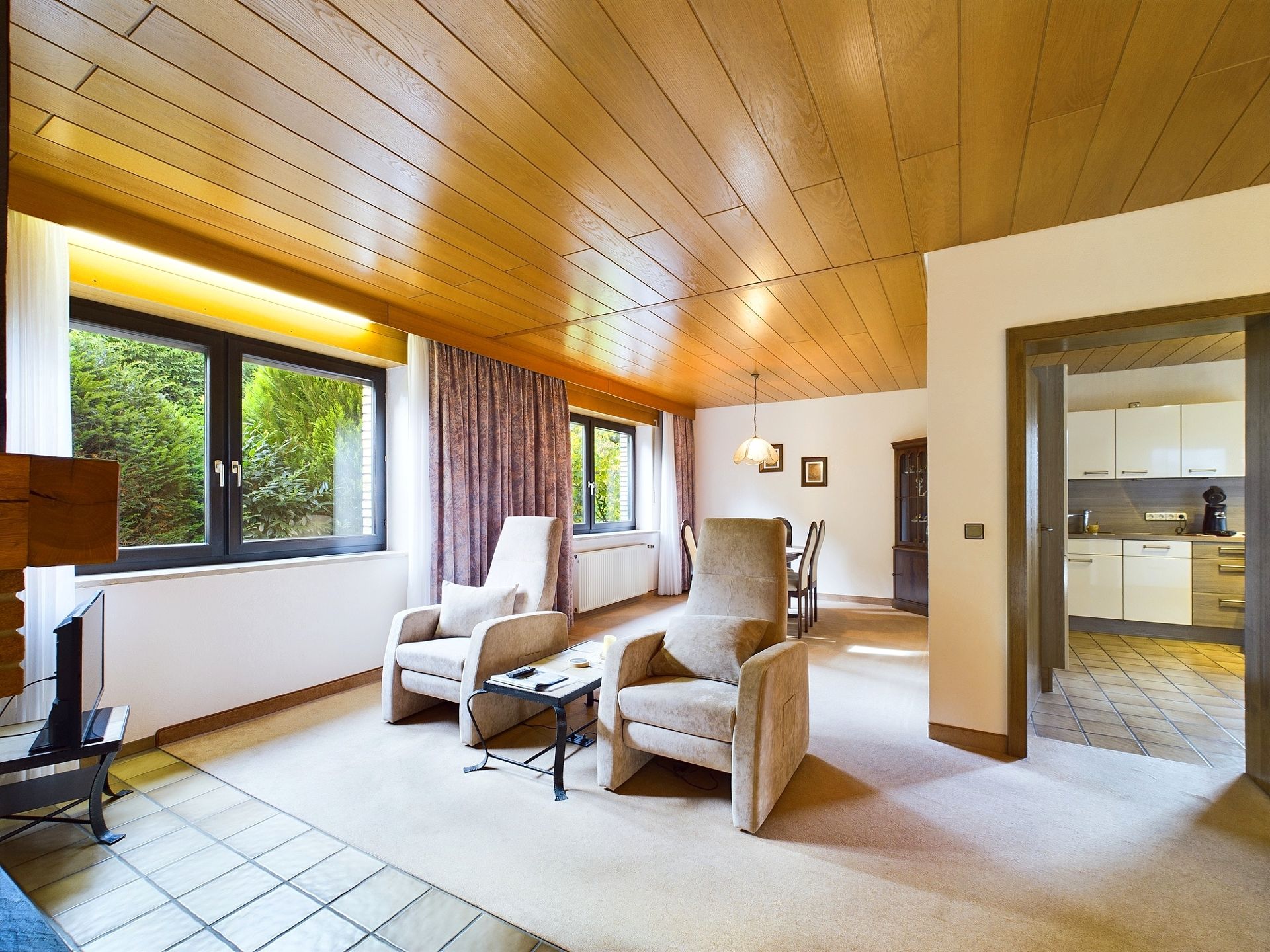 Helles Wohnzimmer mit zwei Sesseln, großem Fenster, Essbereich und Blick in die Küche.