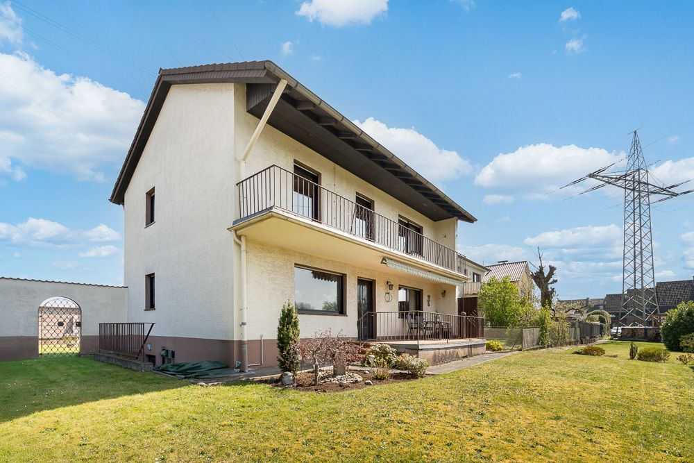 Zweistöckiges Wohnhaus mit Balkon und Garten bei sonnigem Wetter.