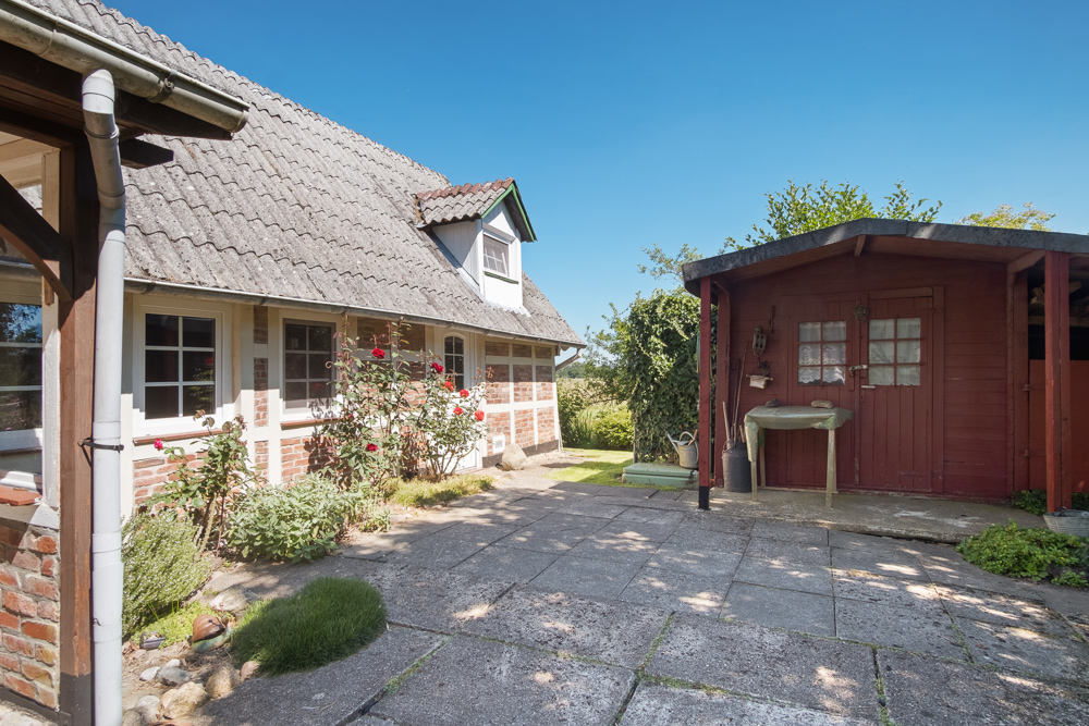 Innenhof mit Blumenbeeten, Pflastersteinen, einem roten Gartenschuppen und einem Haus mit Ziegeldach.