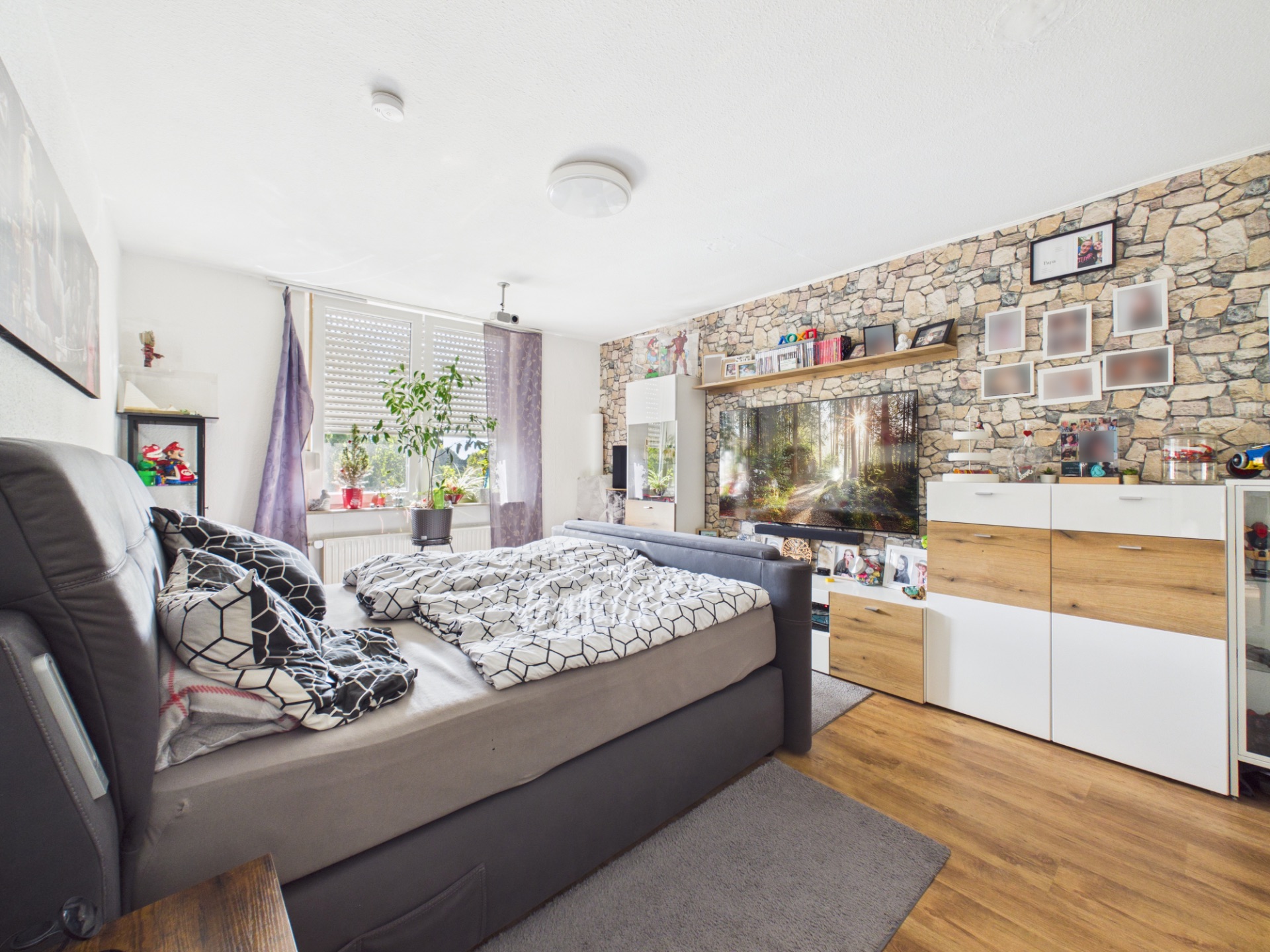 Modernes Schlafzimmer mit großem Bett, Holzboden, Steinwand und Fenster mit Pflanzen.