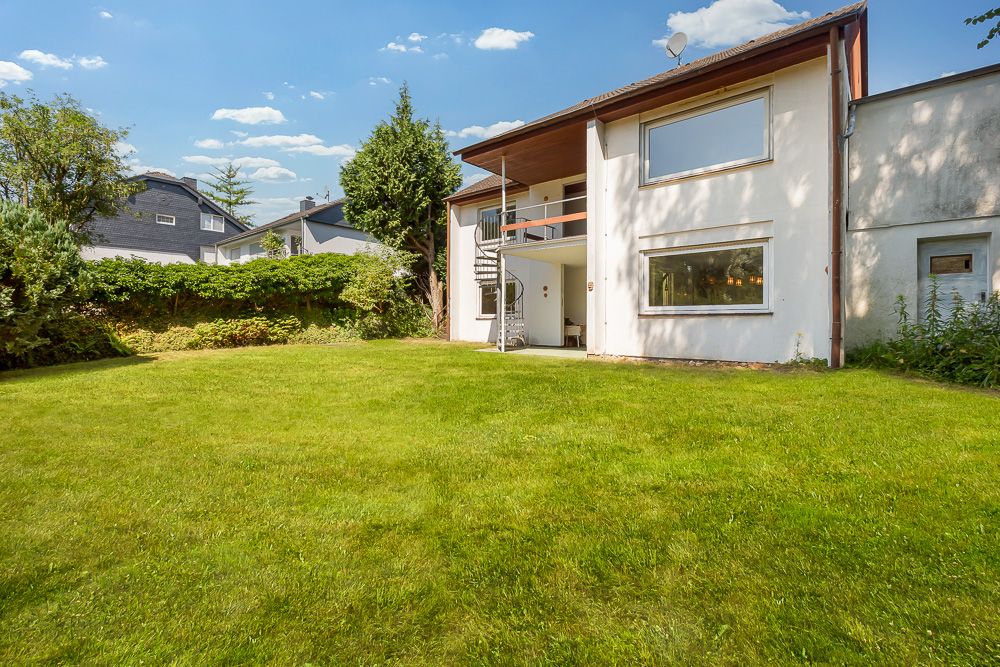 Großer grüner Garten hinter einem weißen Wohnhaus mit Terrasse und Außentreppe.