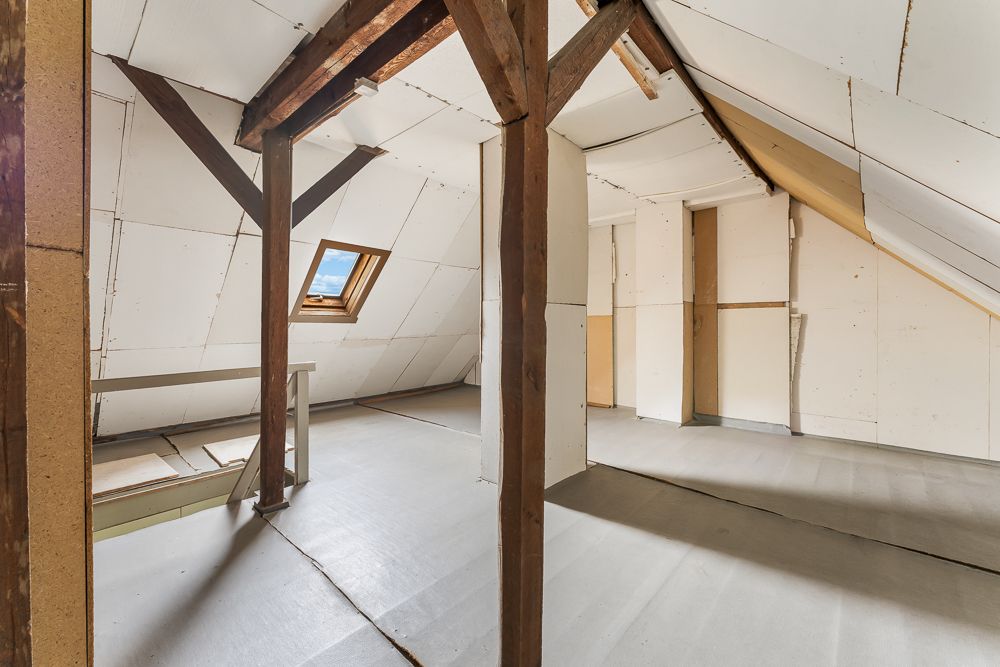 Dachgeschossraum mit sichtbaren Holzbalken, schrägen Wänden und einem Dachfenster.