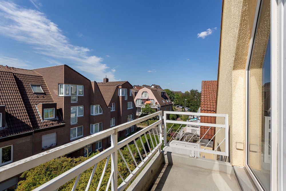 Balkon mit weißem Geländer, Blick auf Nachbarhäuser mit roten Dächern unter blauem Himmel.
