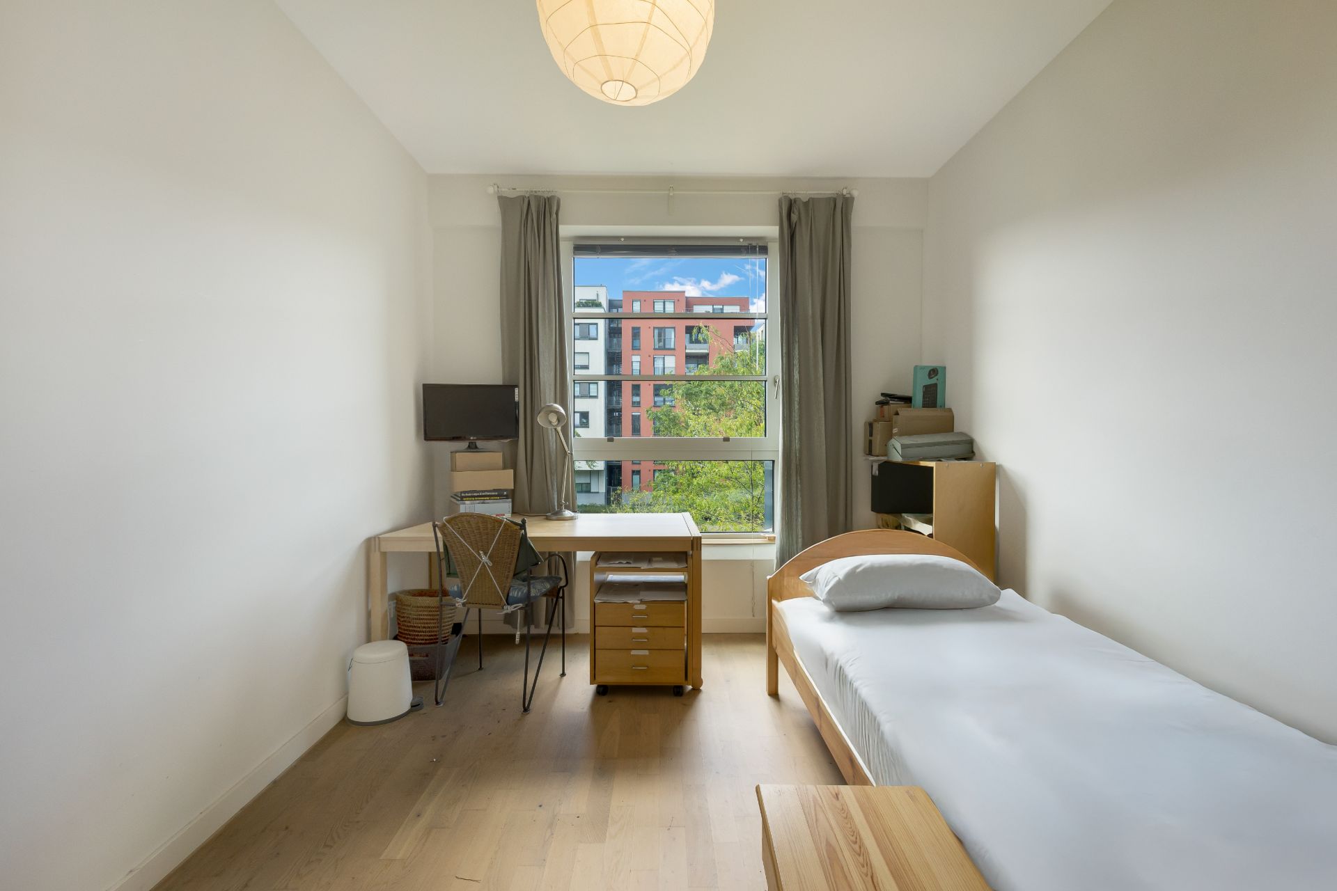 Helles Schlafzimmer mit Einzelbett, Schreibtisch am Fenster und hellem Holzboden.