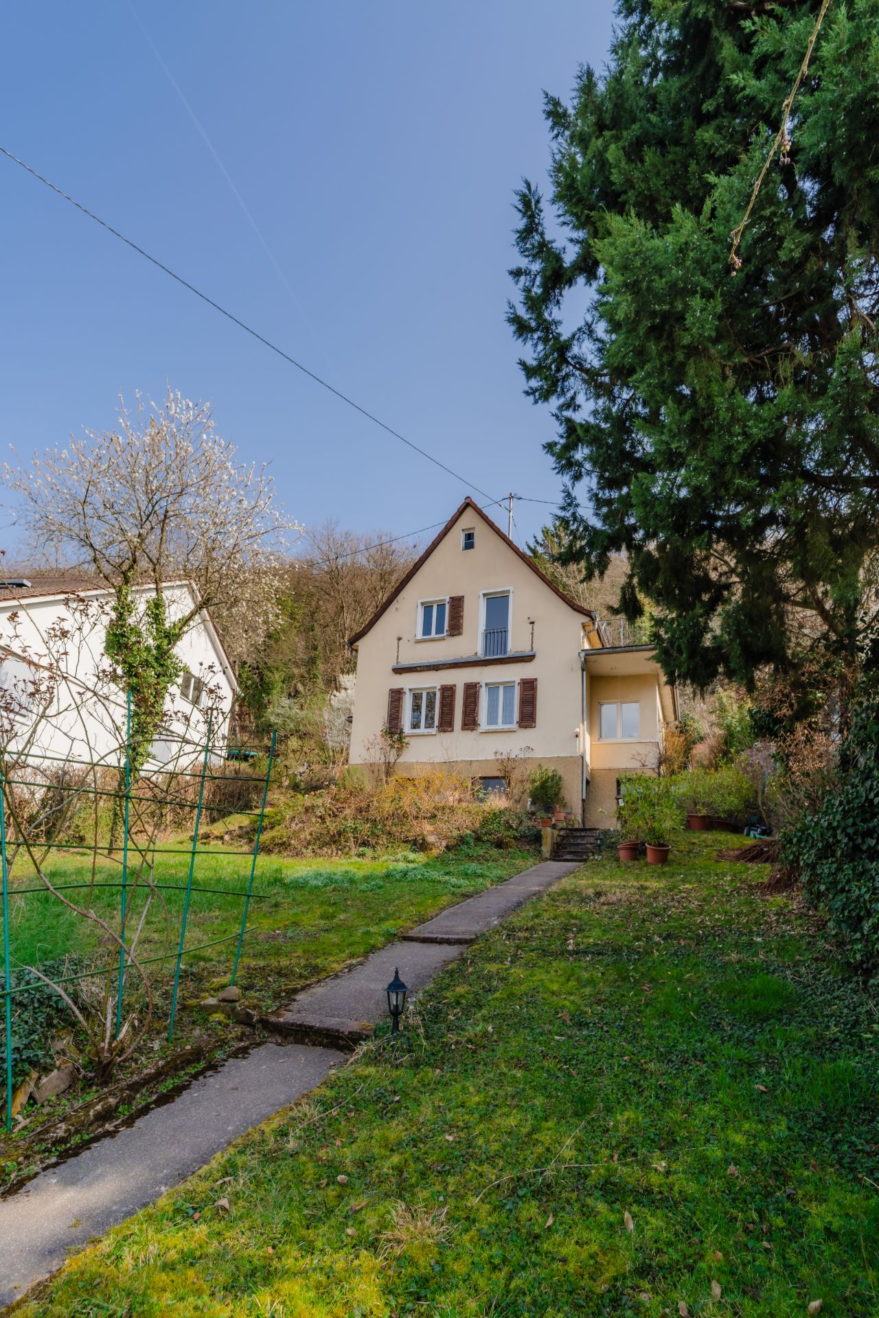 Ein Einfamilienhaus mit braunen Fensterläden und Gartenweg im grünen Vorgarten.