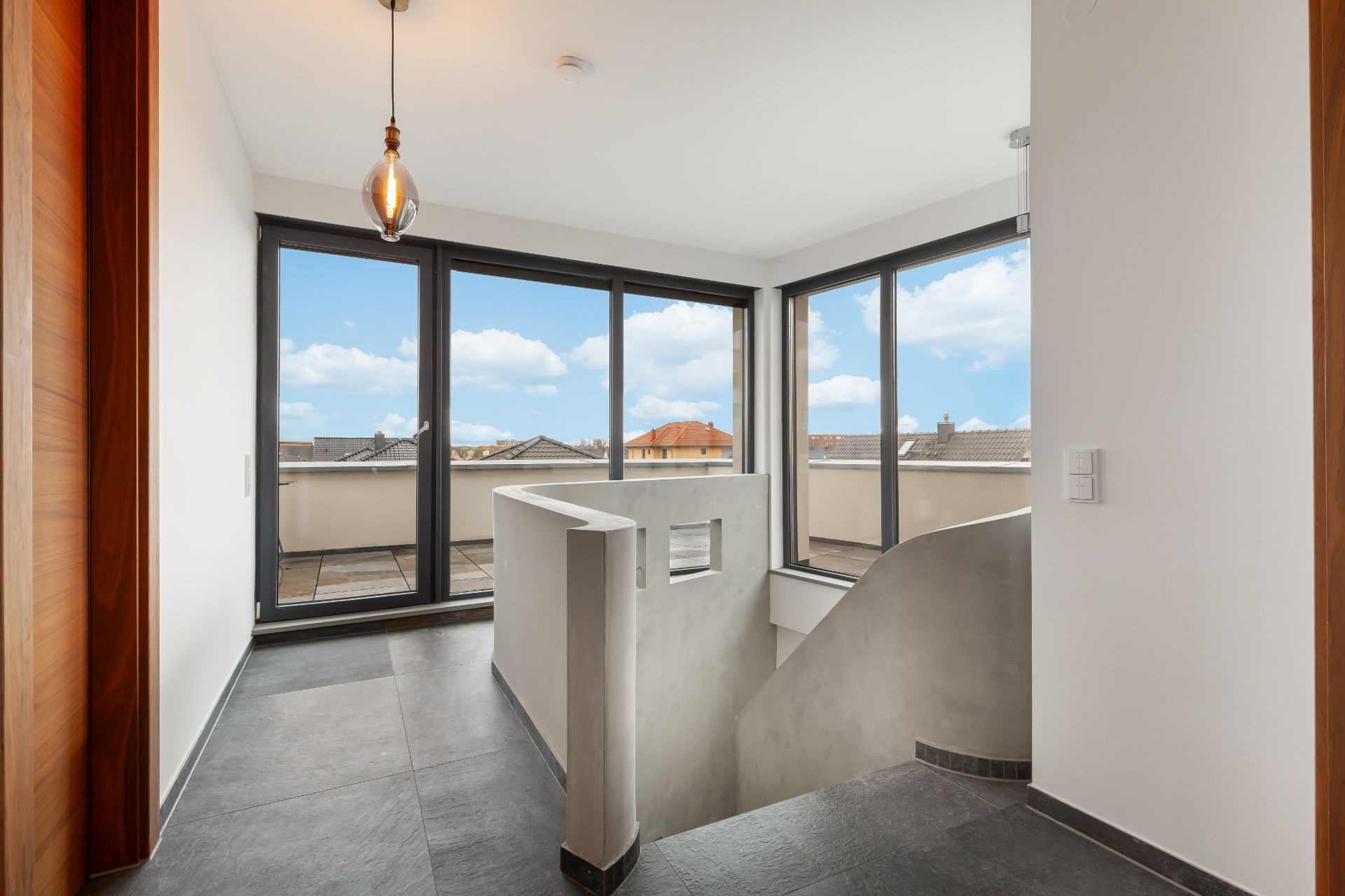 Heller Flur mit großen Fenstern, Blick auf Terrasse und geschwungene Treppe nach unten.