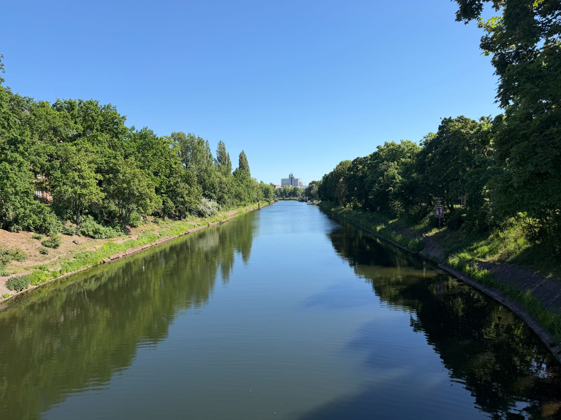 Kanal mit Bäumen an beiden Ufern unter klarem, blauem Himmel.
