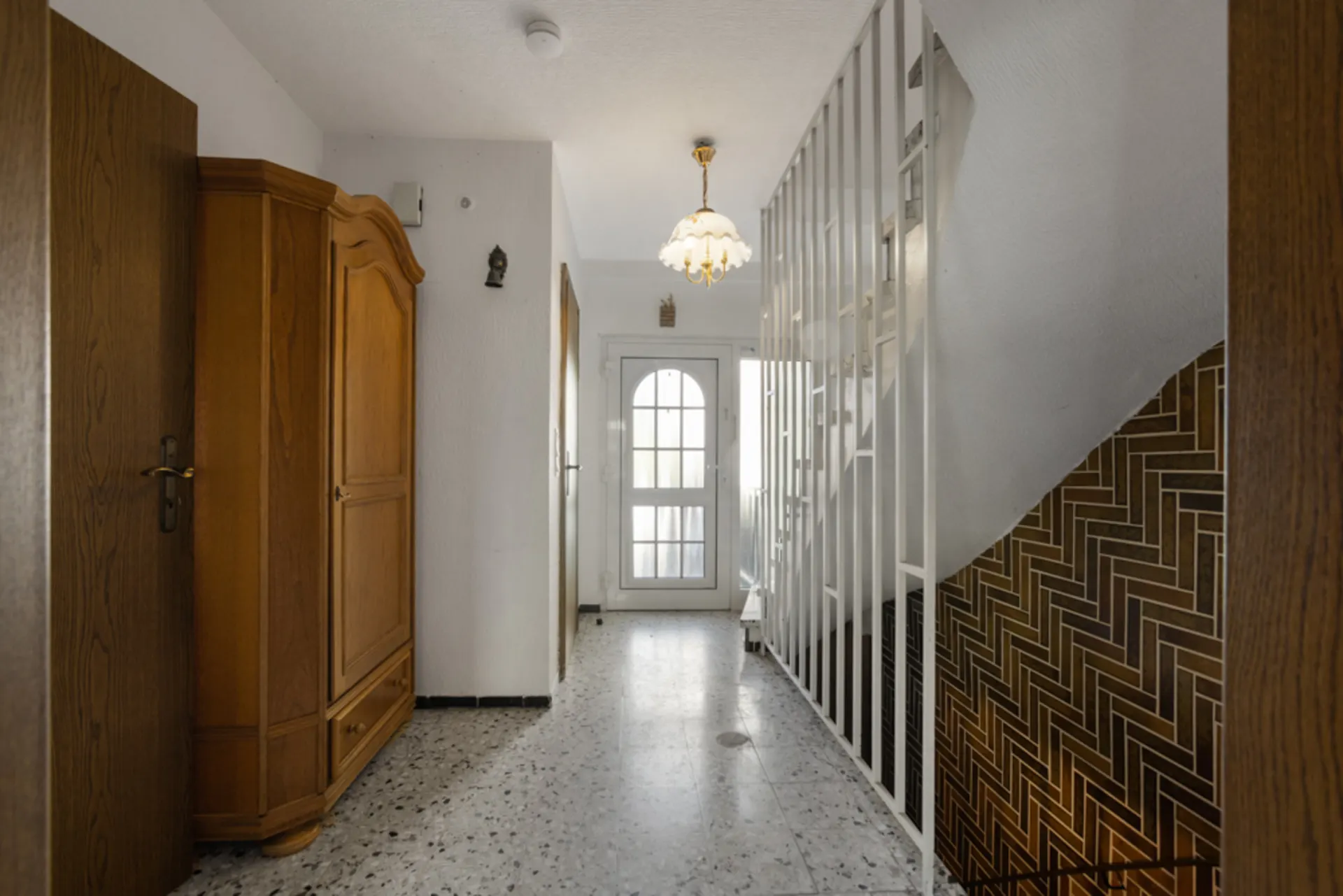Heller Flur mit Holzschrank, Treppe und Glastür, darüber eine Hängelampe.