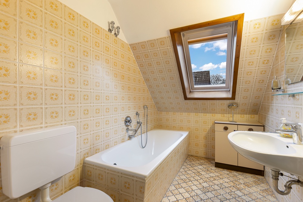 Helles Badezimmer mit Badewanne, Waschbecken, Toilette und Dachfenster unter einer schrägen Decke.