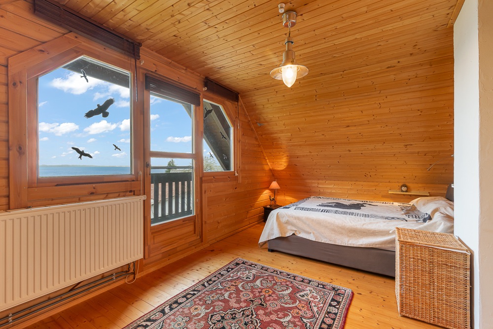 Holzverkleidetes Schlafzimmer mit Doppelbett, Fenster mit Meerblick und Teppich auf dem Boden.