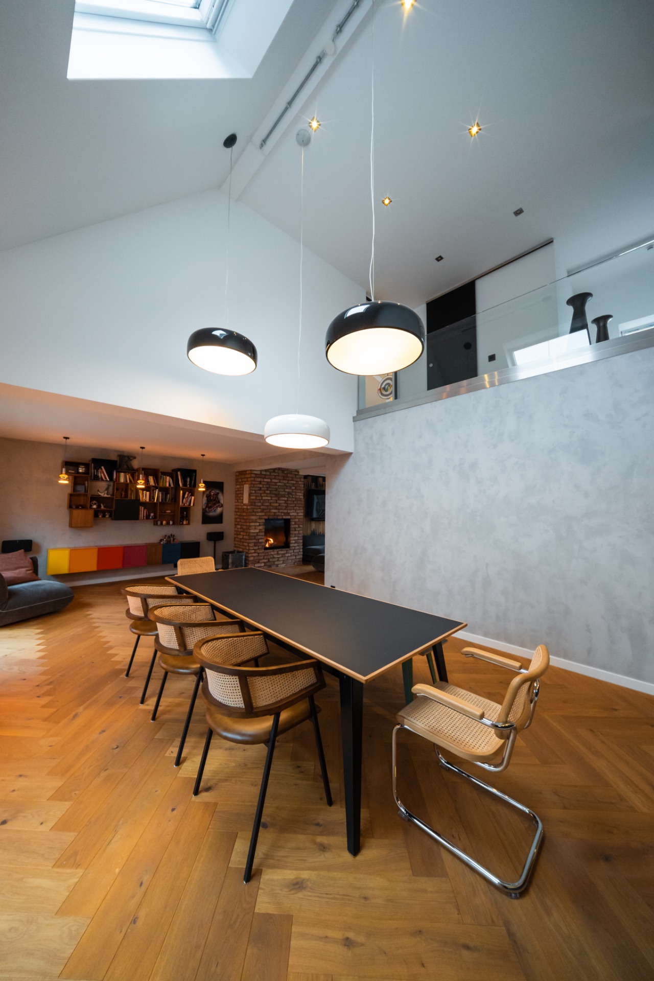 Modernes Esszimmer mit Holzboden, großem Tisch, Stühlen und drei Hängelampen unter Dachfenster.