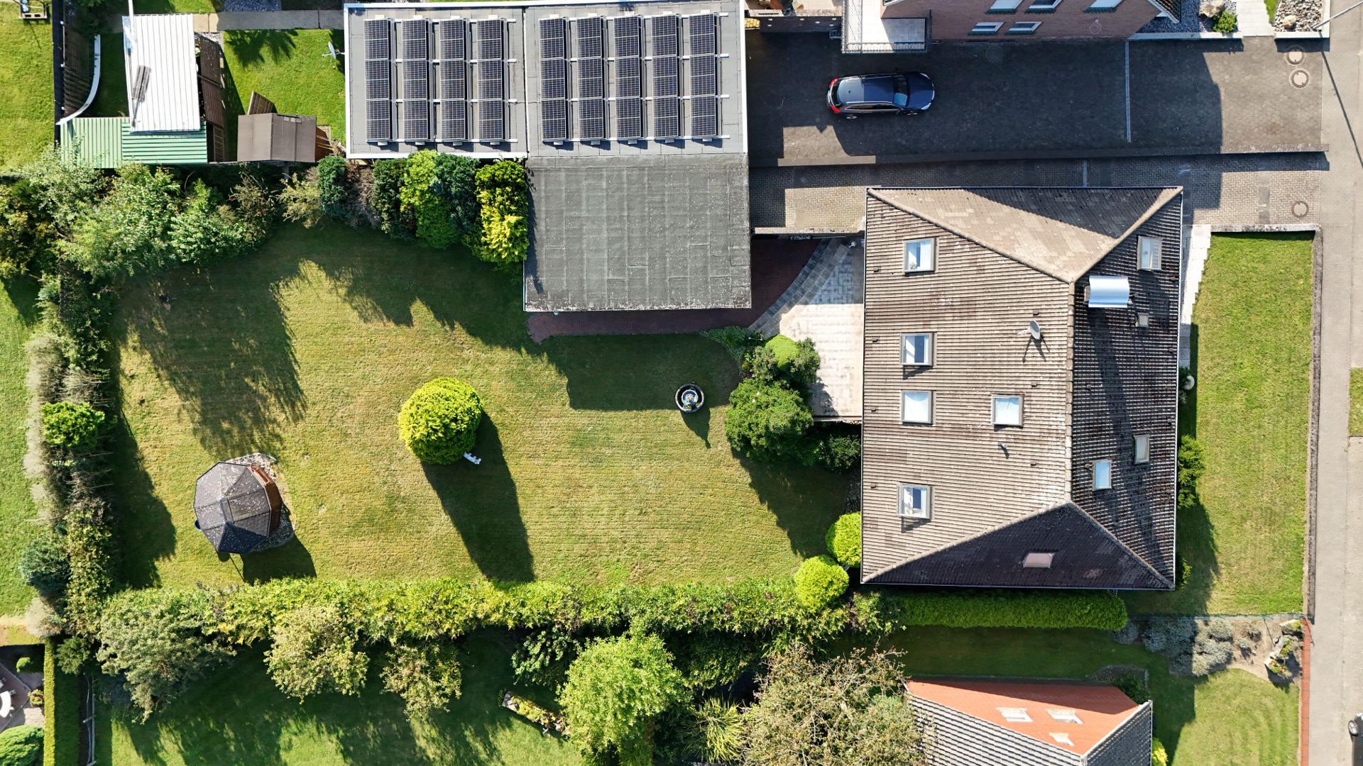 Luftaufnahme eines Hauses mit großem Garten, Rasenfläche, Bäumen und kleinem Pavillon.