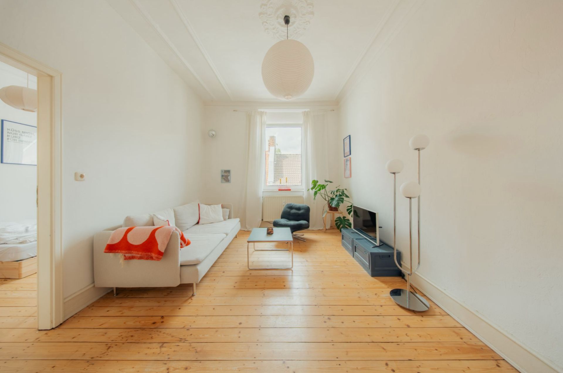 Helles Wohnzimmer mit Holzfußboden, Sofa, Sessel, Couchtisch, Stehlampe und Fernsehtisch.