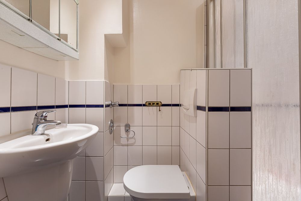 Kleines Badezimmer mit weiß gefliestem Waschbecken, Toilette und Duschkabine.