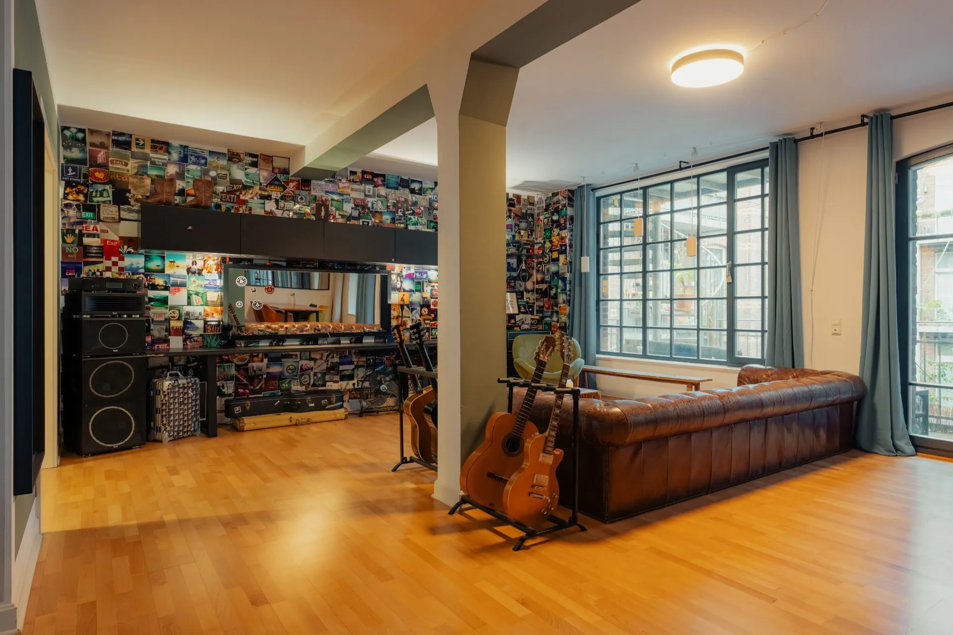 Wohnzimmer mit braunem Ledersofa, Gitarrenständer, großem Fenster und bunt gestalteter Fotowand.