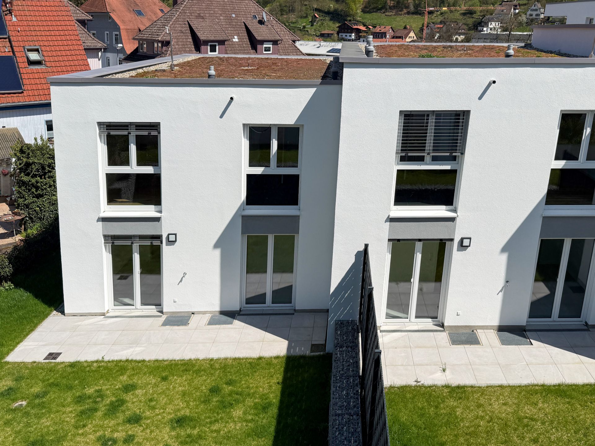 Zwei moderne, weiße Reihenhäuser mit Terrasse und Rasenfläche im Garten.