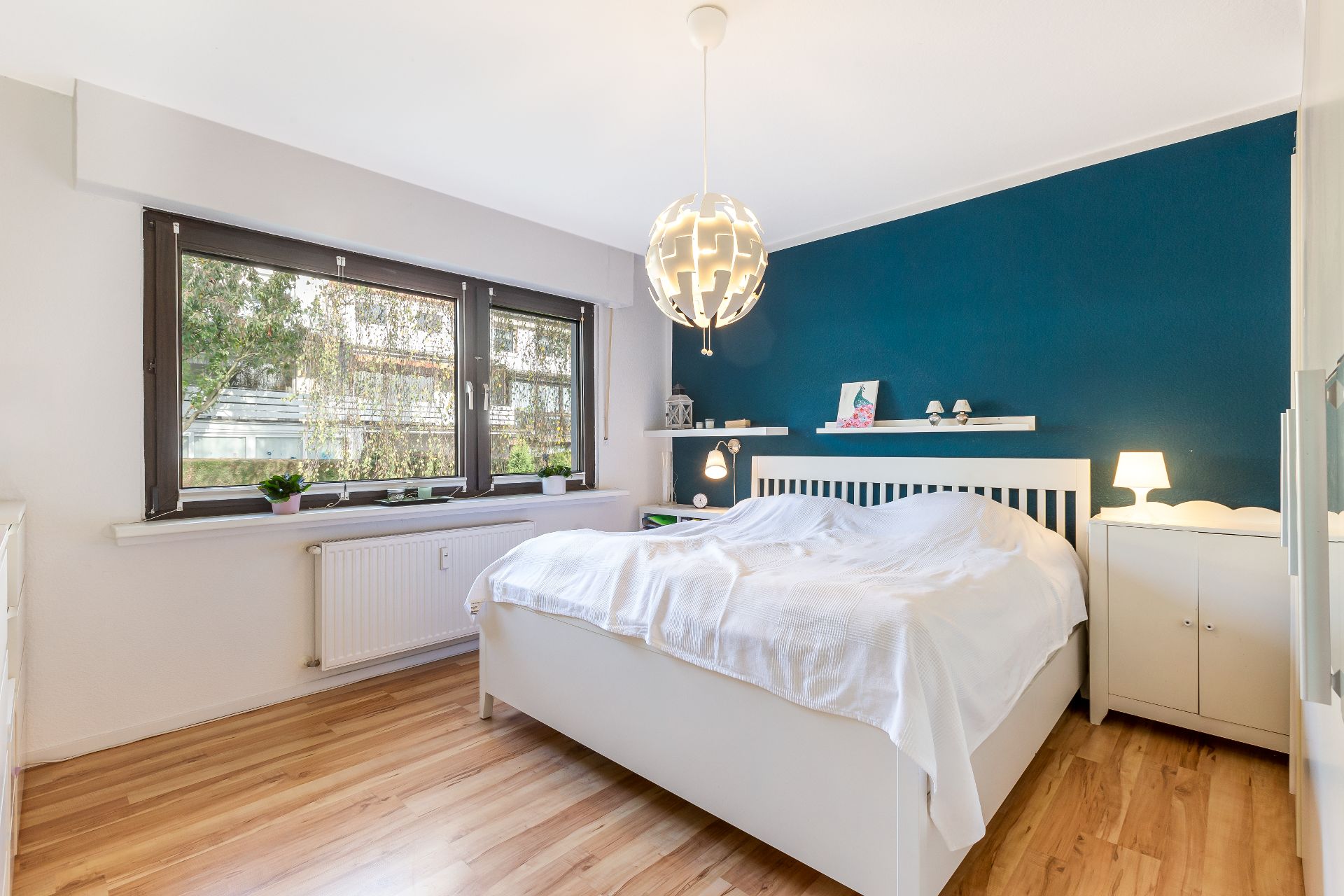 Helles Schlafzimmer mit großem Bett, Holzfußboden und blauer Akzentwand.