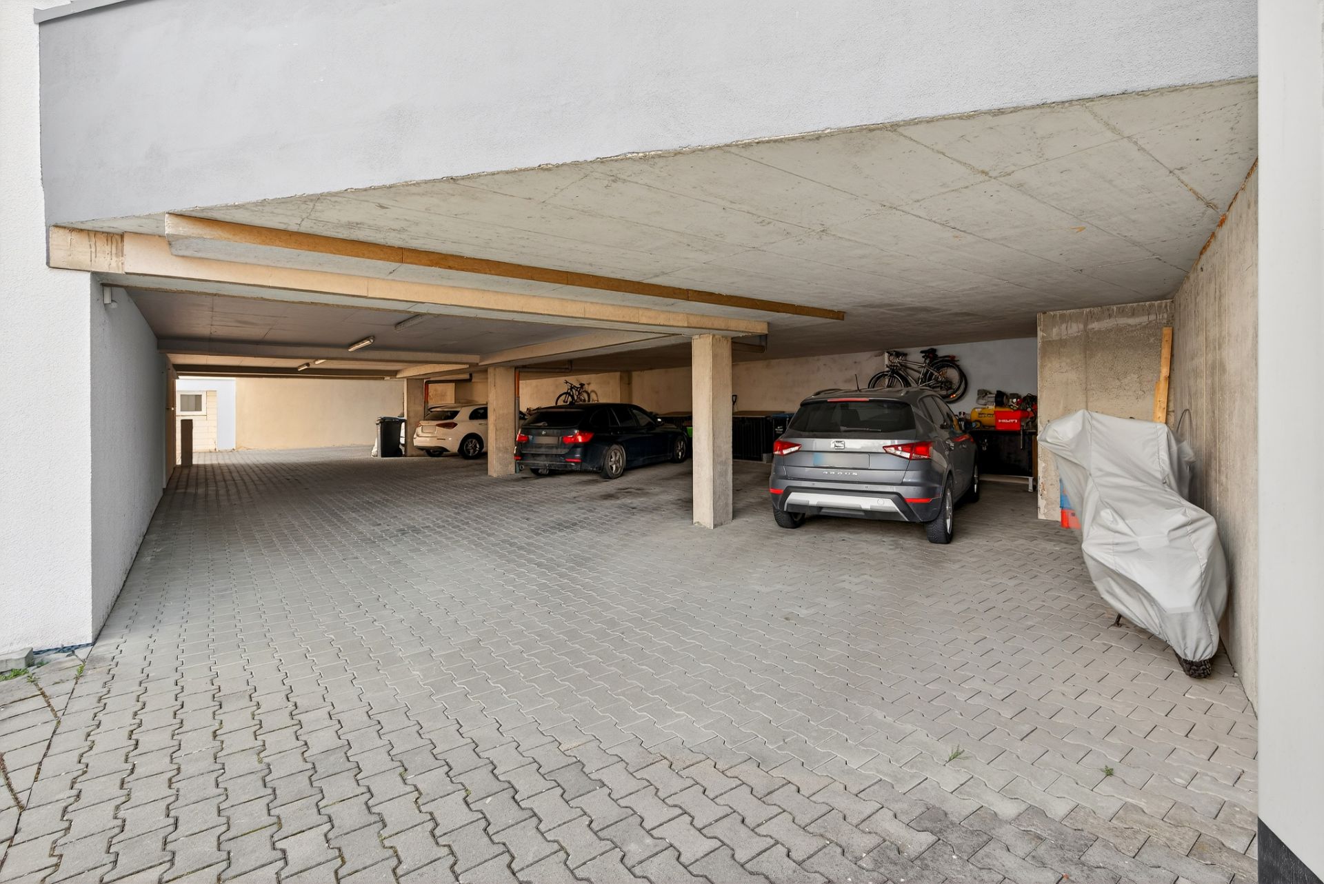 Überdachter Parkplatz mit mehreren Autos und einigen Fahrrädern an der Wand.
