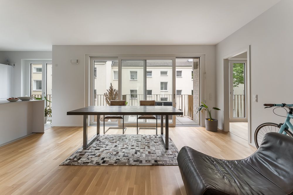 Helles Wohnzimmer mit Esstisch, Stühlen, Teppich und Zugang zum Balkon, moderne Einrichtung.