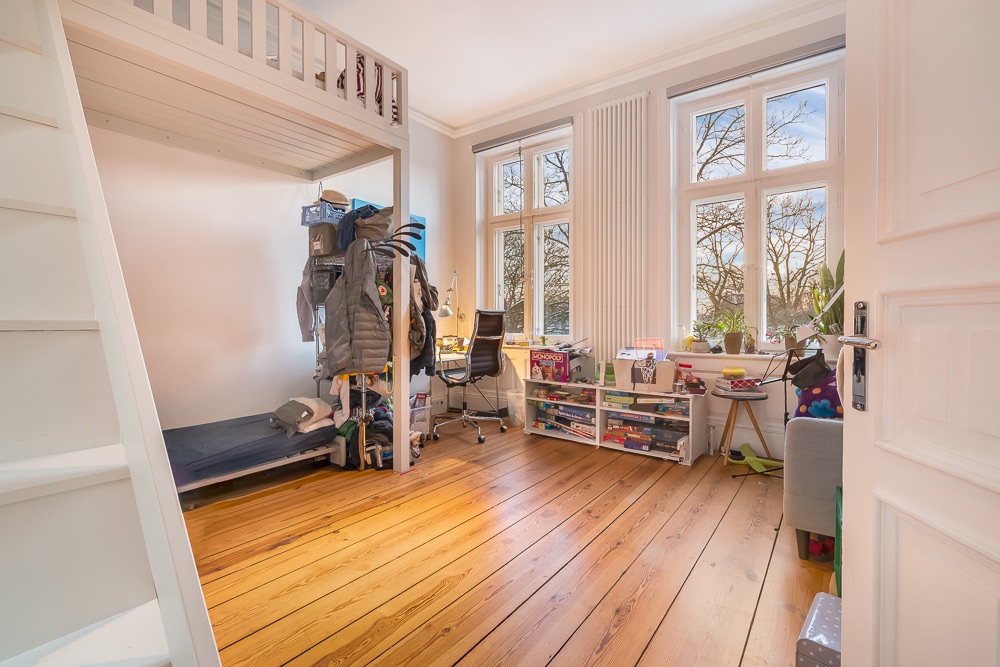 Helles Kinderzimmer mit Hochbett, Schreibtisch, Regalen und großen Fenstern mit Blick nach draußen.