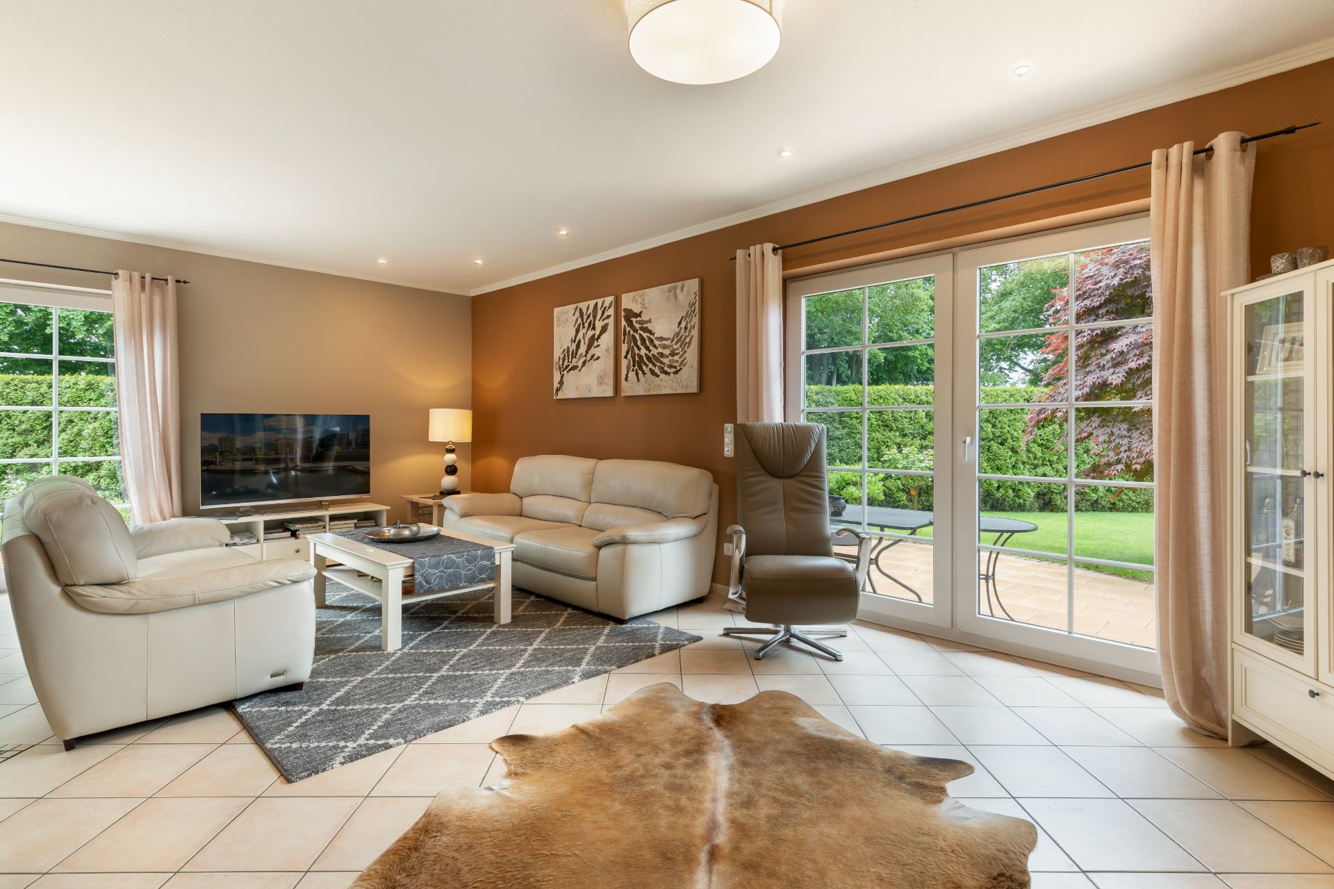 Modernes Wohnzimmer mit Ledersofas, Fernseher, großem Fenster und Blick auf den Garten.