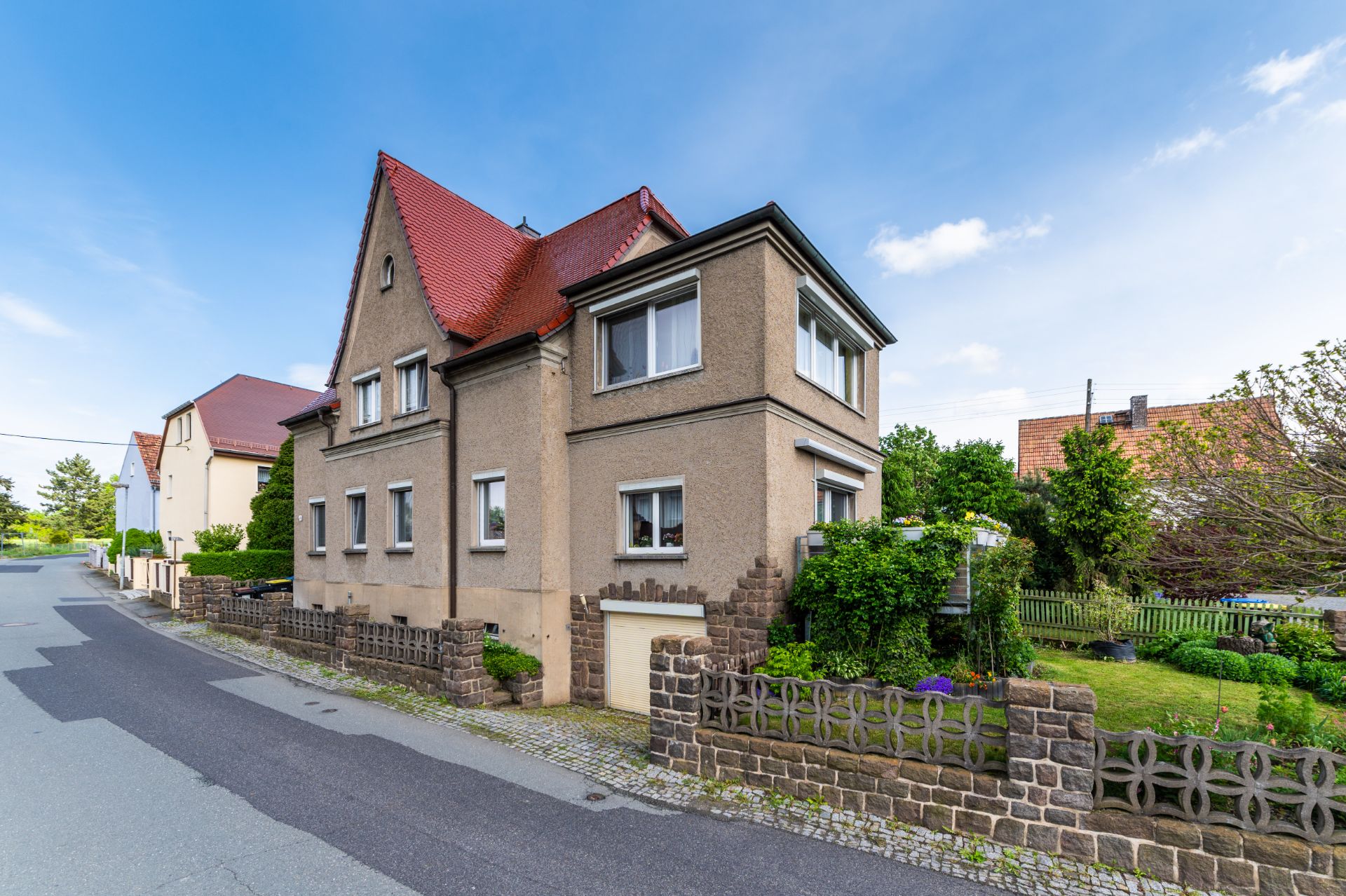 Zweistöckiges Wohnhaus mit rotem Dach und kleinem Vorgarten an einer ruhigen Straße.