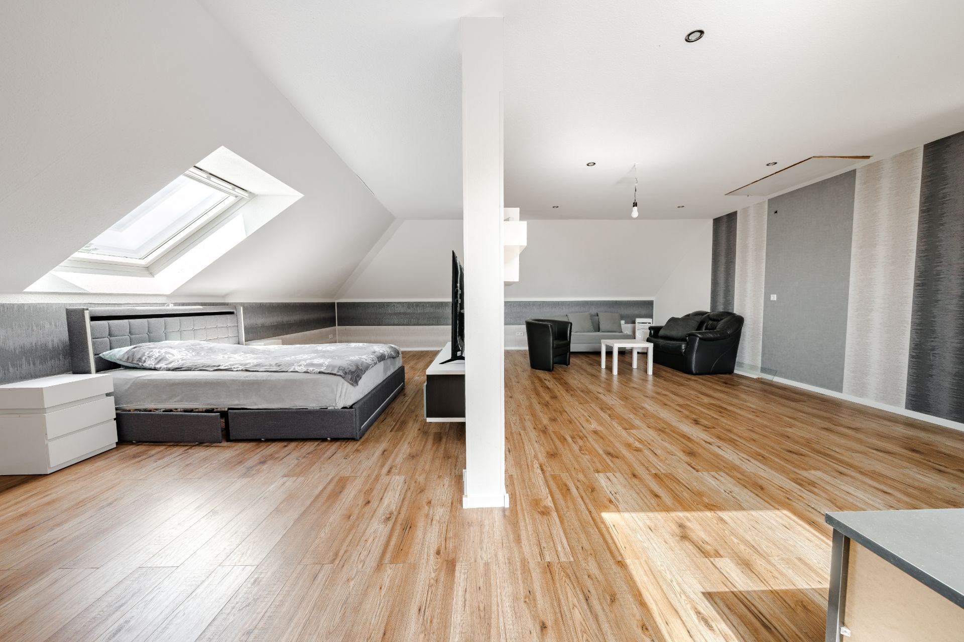 Helles Dachzimmer mit Bett, Sofa, Tisch und Holzfußboden.
