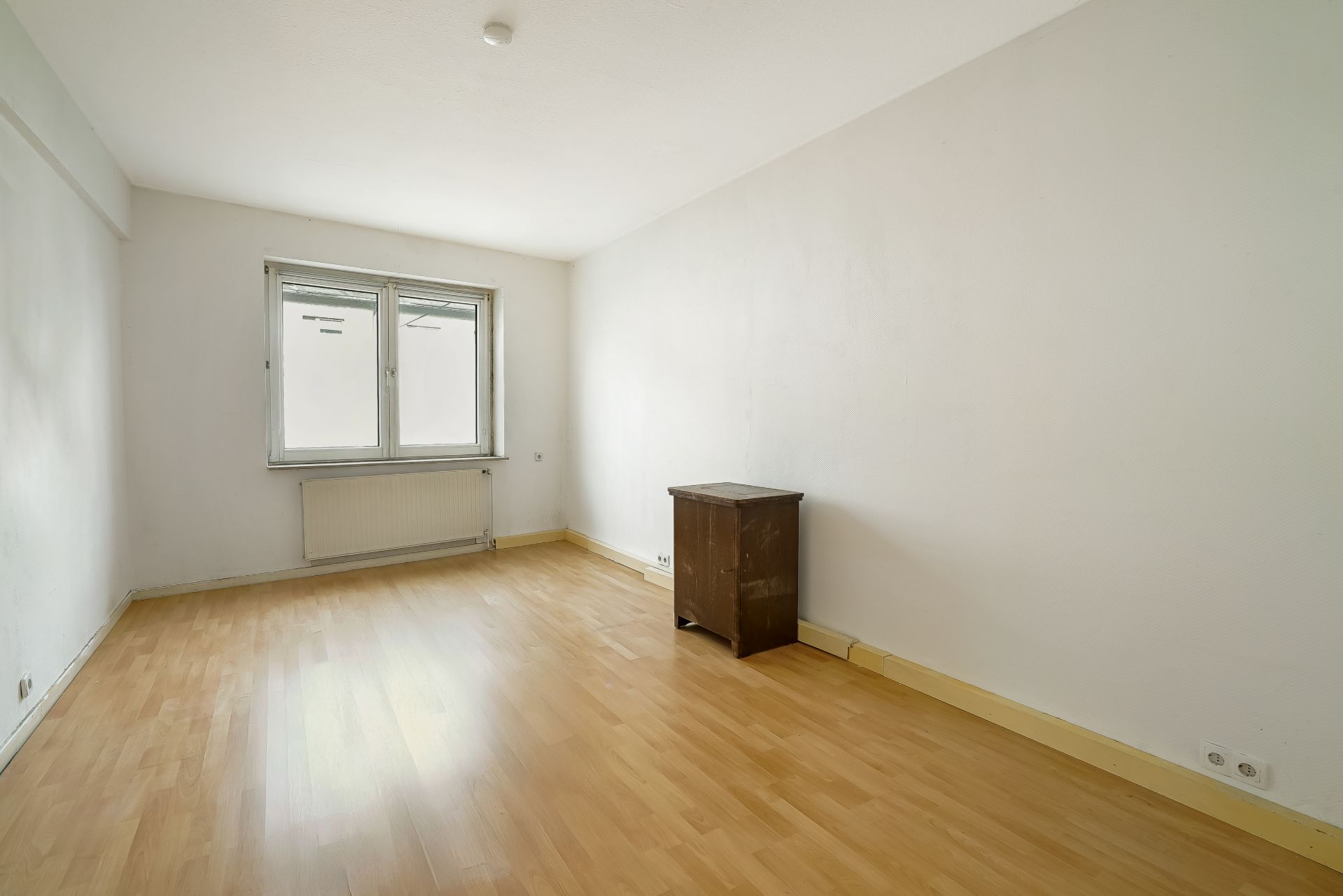 Leerer Raum mit Holzfußboden, weißer Wand, Fenster und kleinem Schrank.