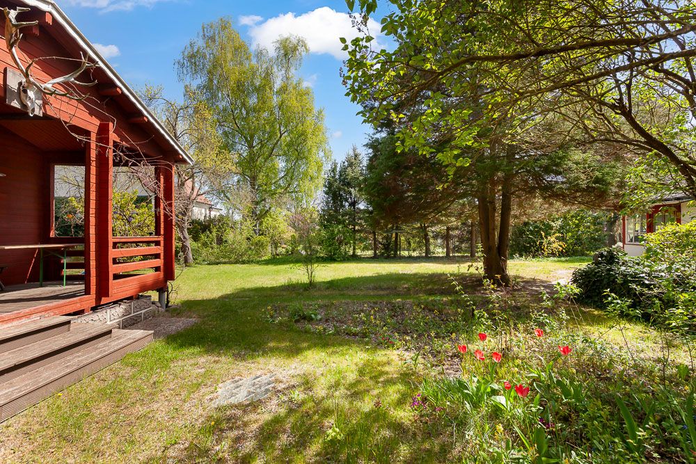 Garten mit Rasen, Bäumen und Blumenbeet neben einer Holzveranda eines Hauses.