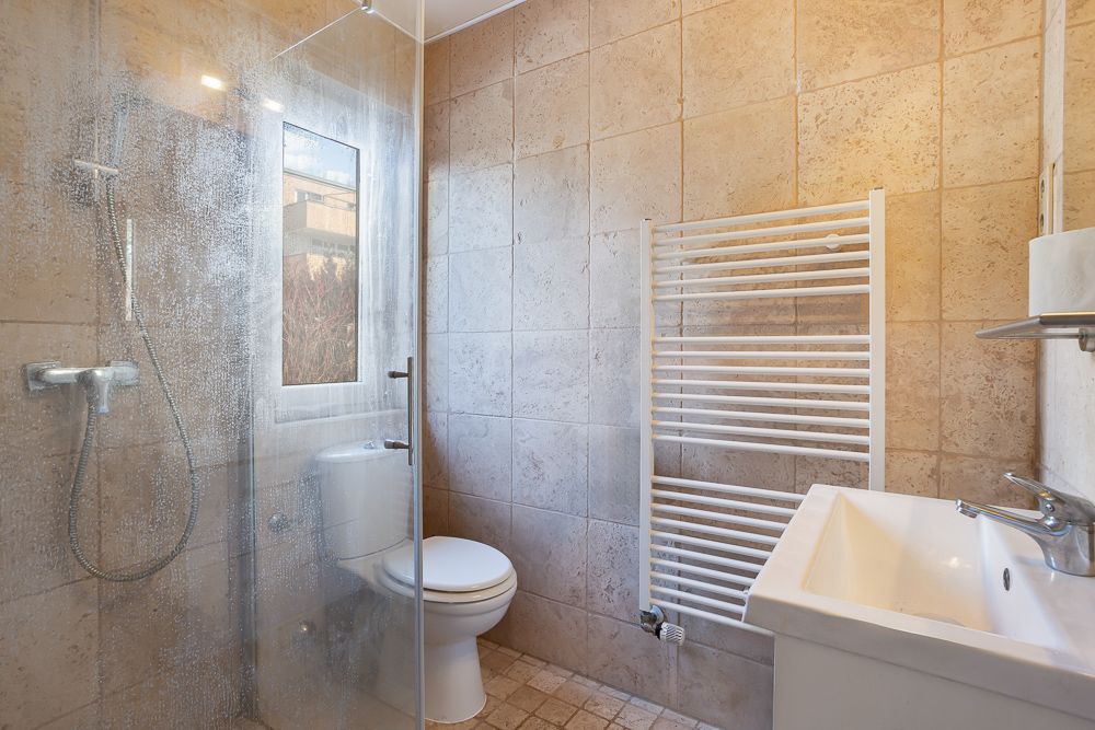 Modernes Bad mit Dusche, WC, Waschbecken und Handtuchheizkörper.
