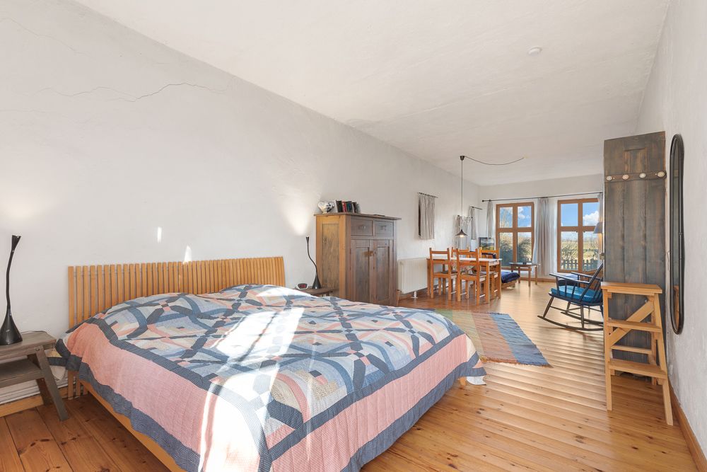 Helles Schlafzimmer mit Holzboden, Doppelbett, Schrank, Esstisch und großen Fenstern.