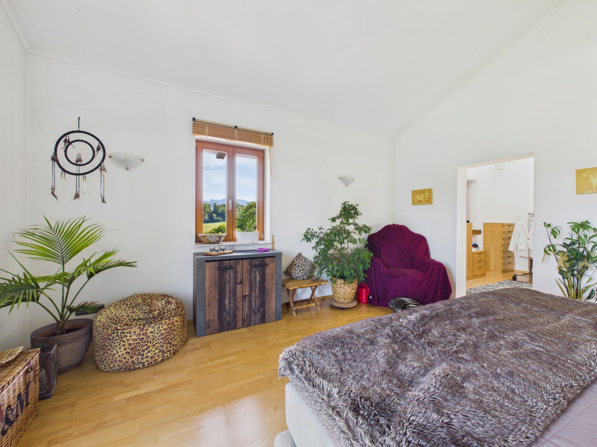 Helles Schlafzimmer mit Pflanzen, einem Fenster, Sitzgelegenheiten und einem Bett mit Felldecke.