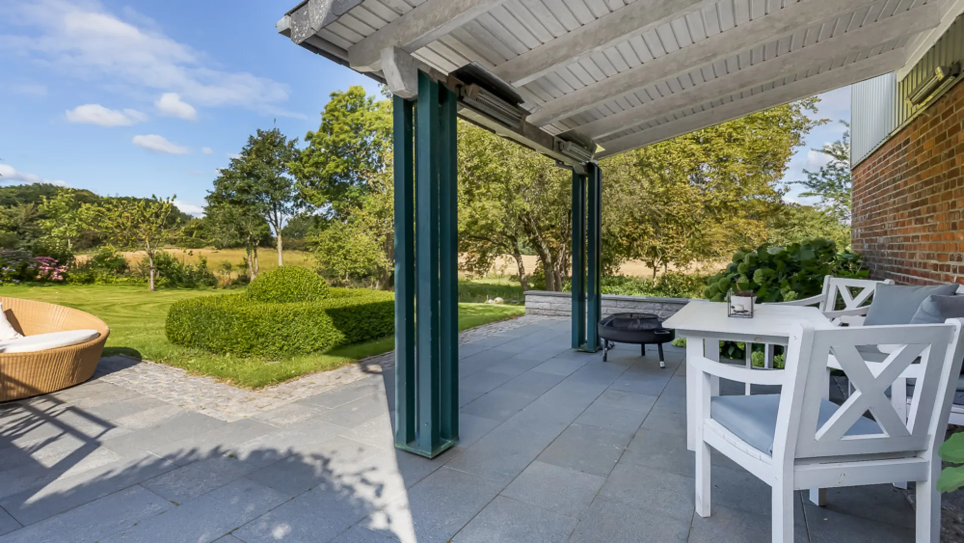 Überdachte Terrasse mit weißen Gartenmöbeln und Blick auf einen grünen Garten.