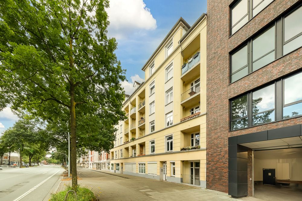 Mehrstöckiges Wohnhaus mit Balkonen an einer Baumallee und breitem Gehweg.