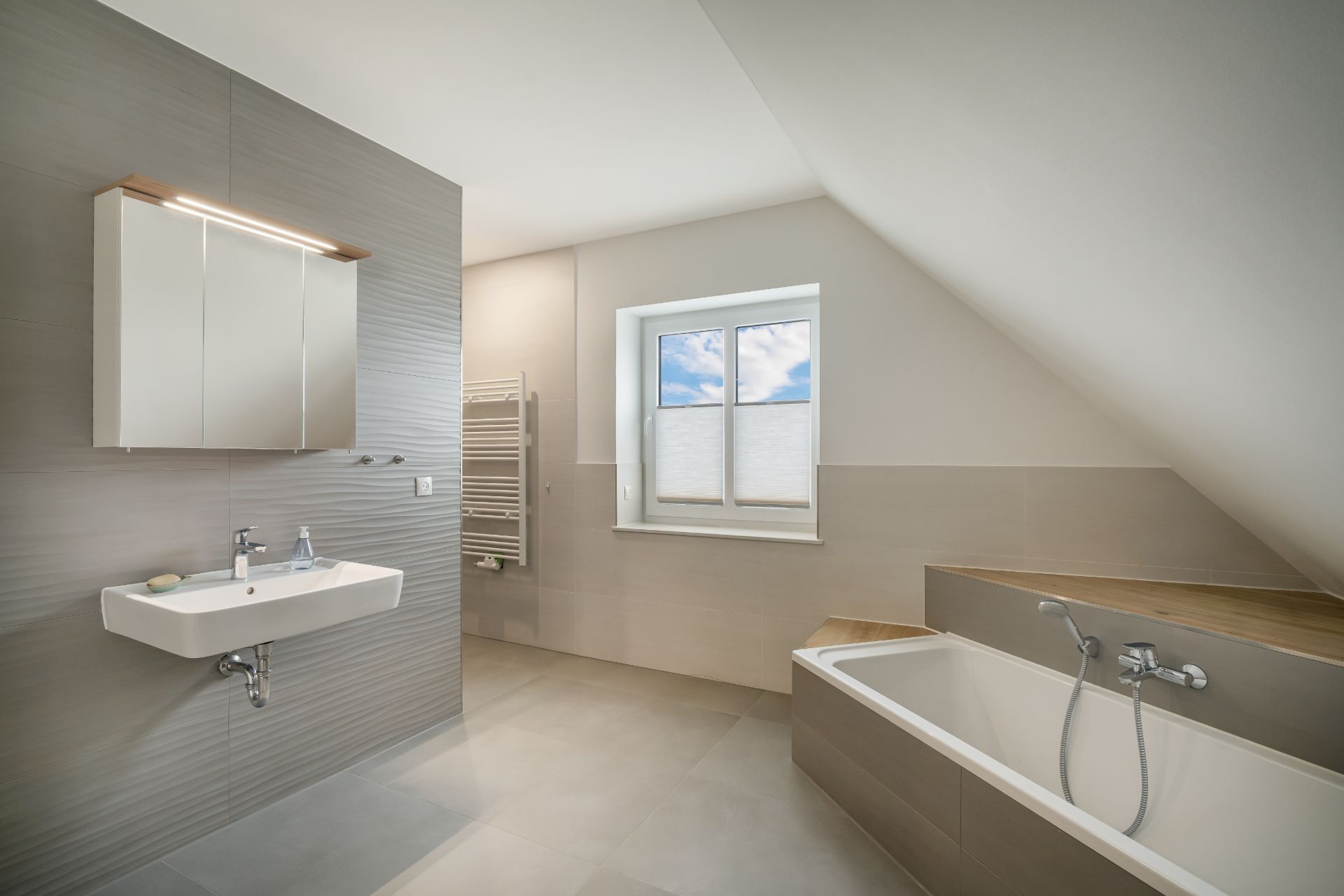 Modernes Badezimmer mit Badewanne, Waschbecken und großem Fenster unter einer Dachschräge.