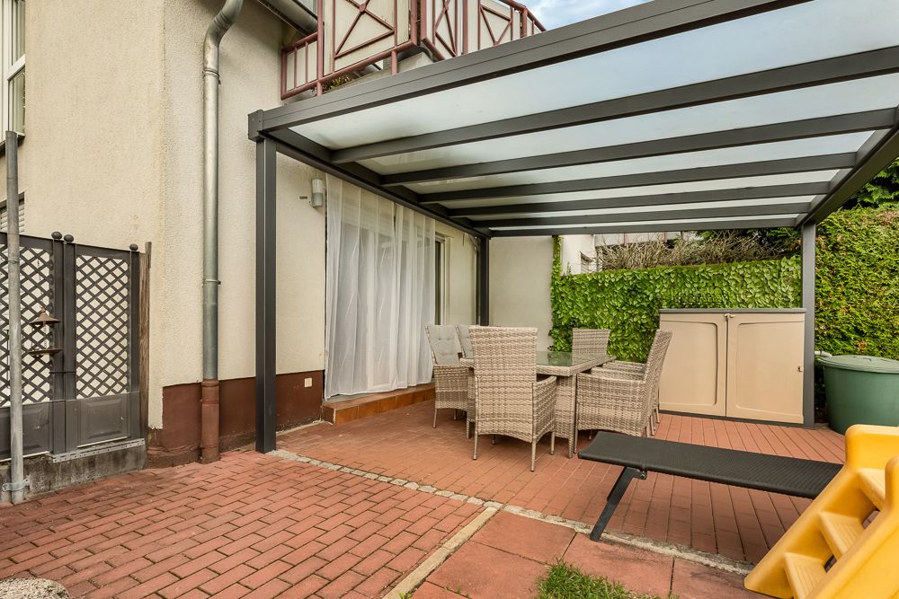 Überdachte Terrasse mit Esstisch, Stühlen und Gartenmöbeln an einem Wohnhaus.