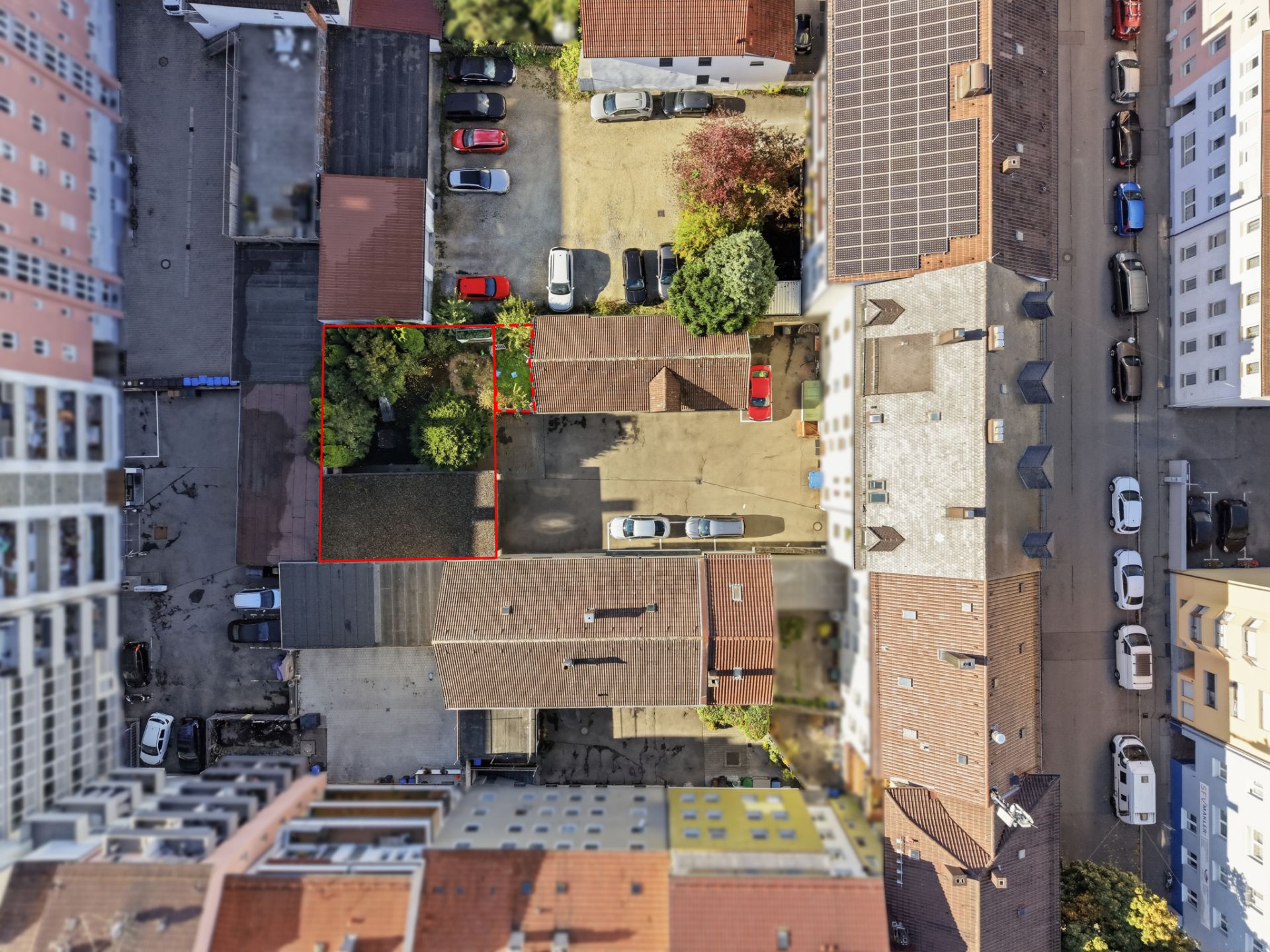 Luftaufnahme eines Innenhofs mit mehreren Häusern, Straßen und geparkten Autos, Bereich rot markiert.