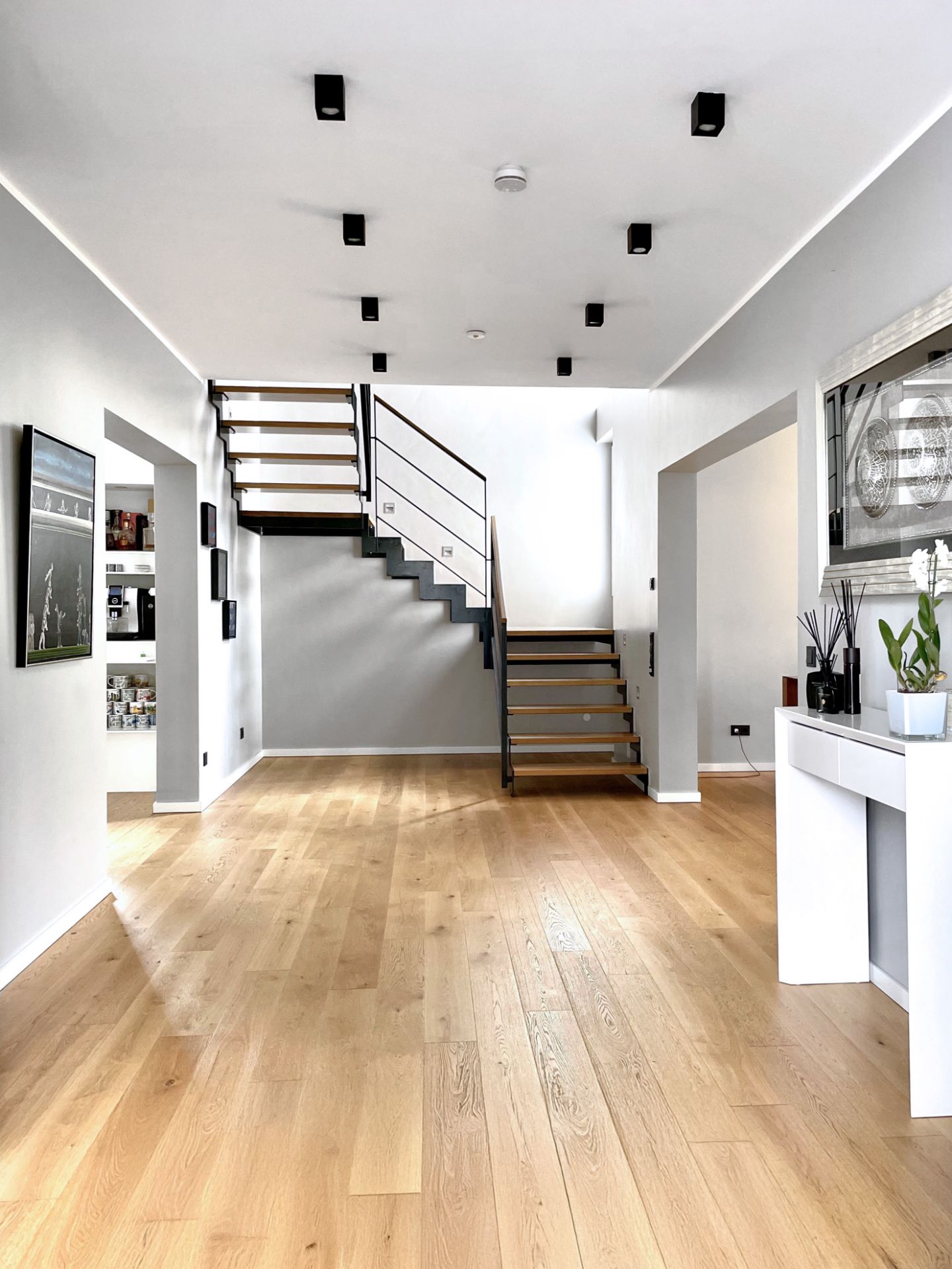Helles Wohnzimmer mit Holzfußboden, moderner Treppe und Dekoration auf weißem Tisch.