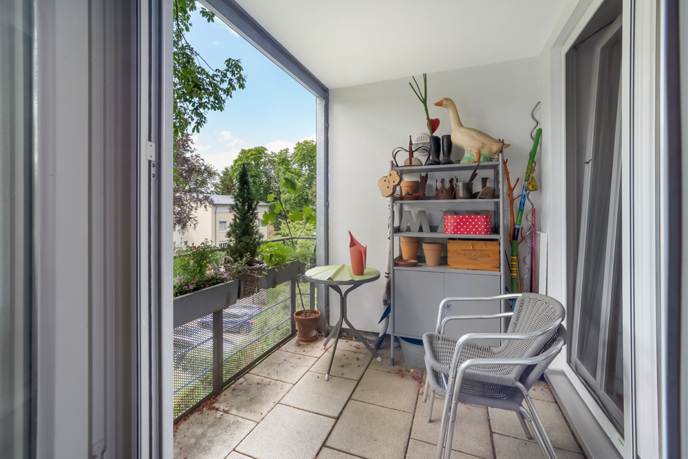 Kleiner Balkon mit zwei Stühlen, kleinem Tisch und Regal mit Töpfen und Dekoration.